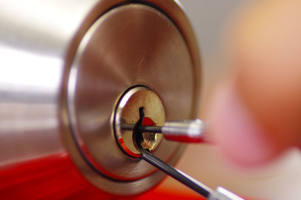 Two lock picks inserted into a silver door lock, with a hand holding one pick — Terrace Locksmiths in Raymond Terrace, NSW