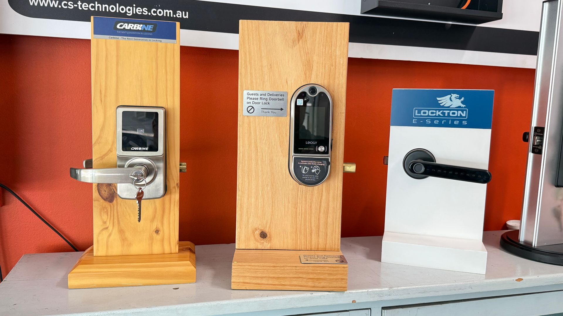 Three electronic door lock display units on a counter, including silver and black keypad models and a blue sign— Terrace Locksmiths in Raymond Terrace, NSW