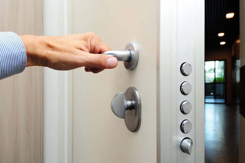 Hand Pressing a Silver Doorbell Panel Beside a White Door — Terrace Locksmiths in Raymond Terrace, NSW