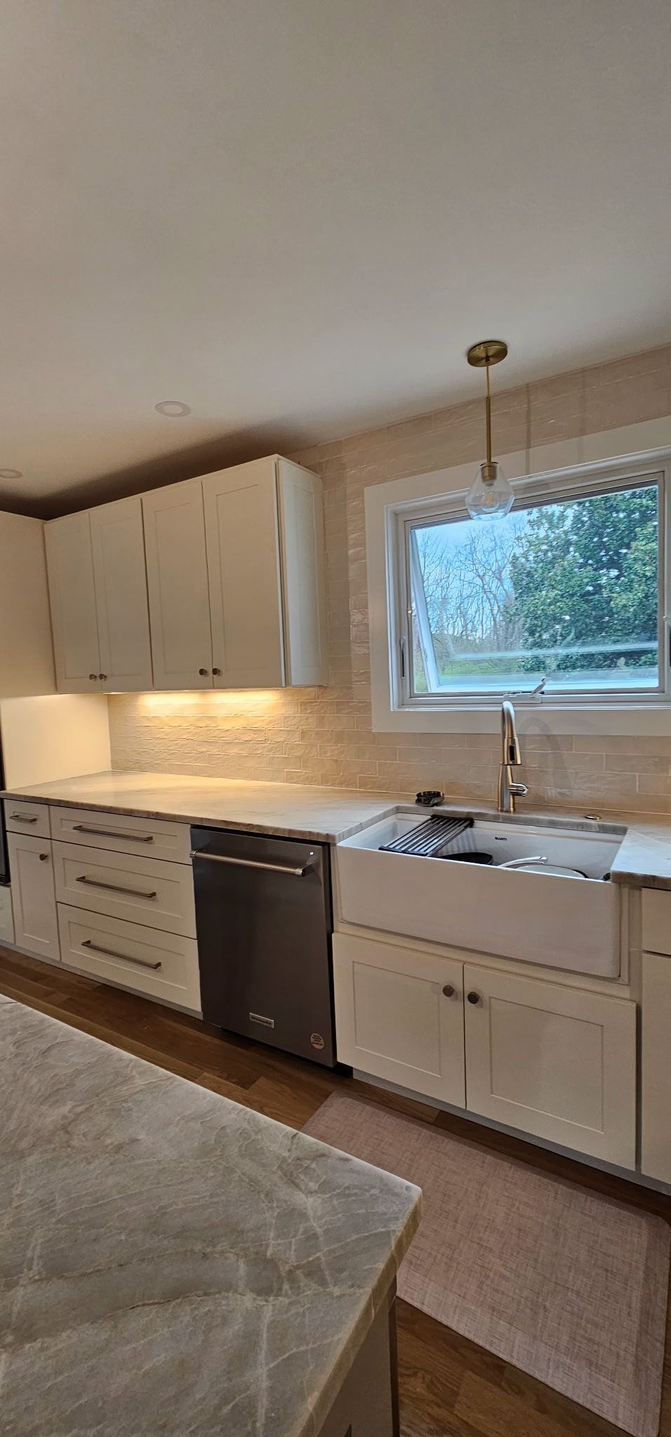 A kitchen with white cabinets , a sink , a dishwasher , and a window.