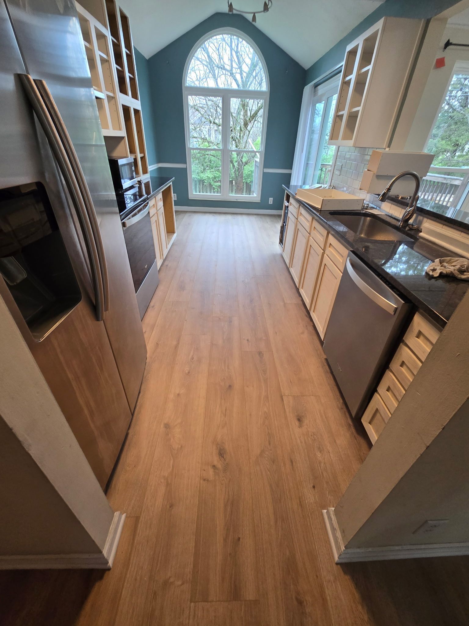 A kitchen with hardwood floors , stainless steel appliances , and a large window.