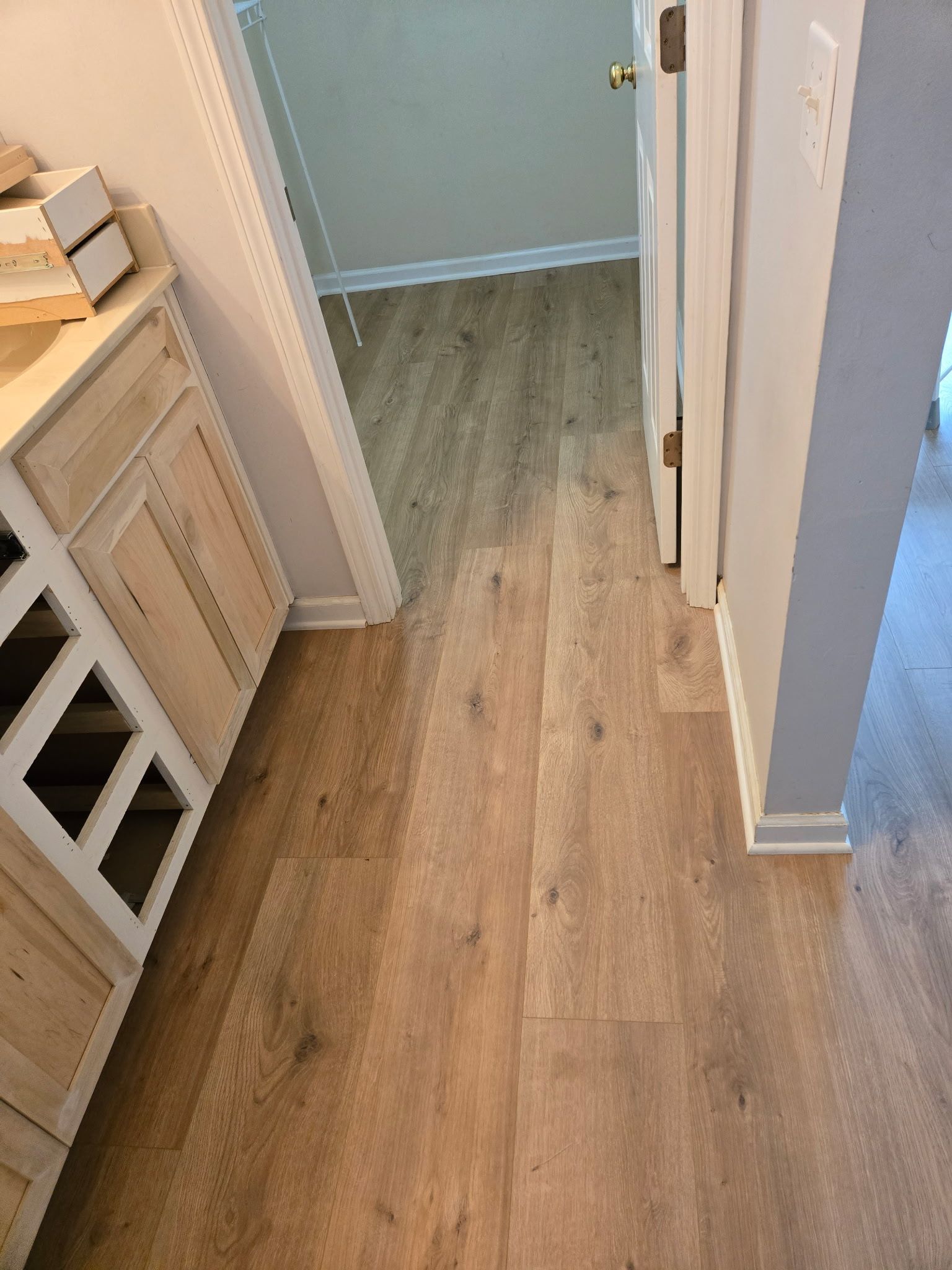 A hallway with hardwood floors leading to a bathroom.