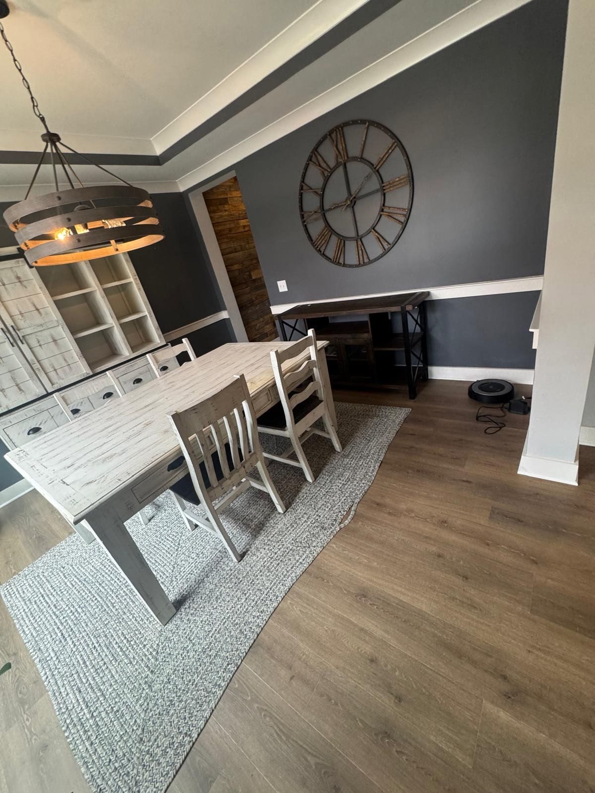 A dining room with a table and chairs and a clock on the wall.