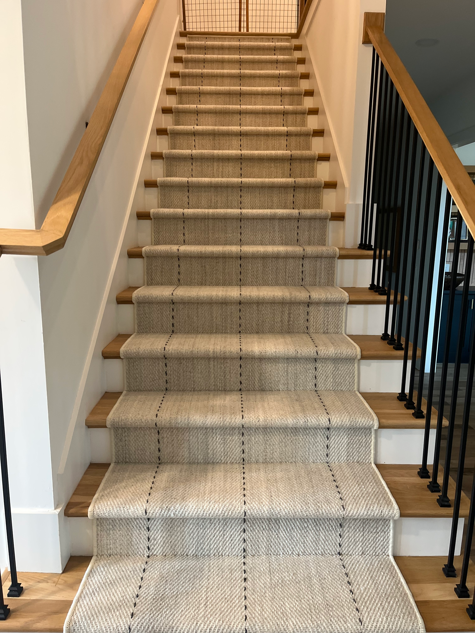 Carpeted indoor staircase with wooden handrails and black iron balusters, viewed from the bottom.