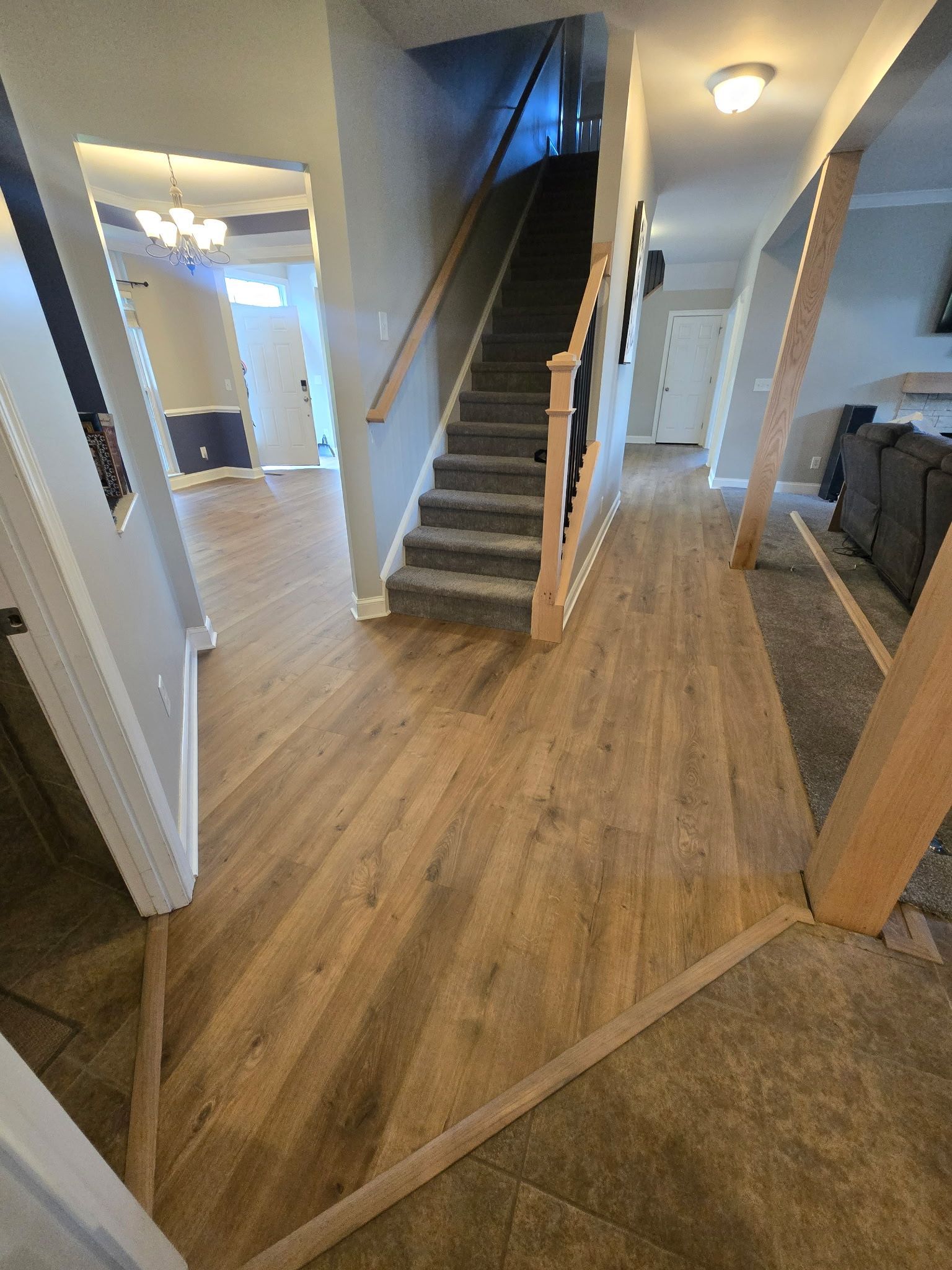 Entryway with wood floors, stairs, and view into living room with chandelier.