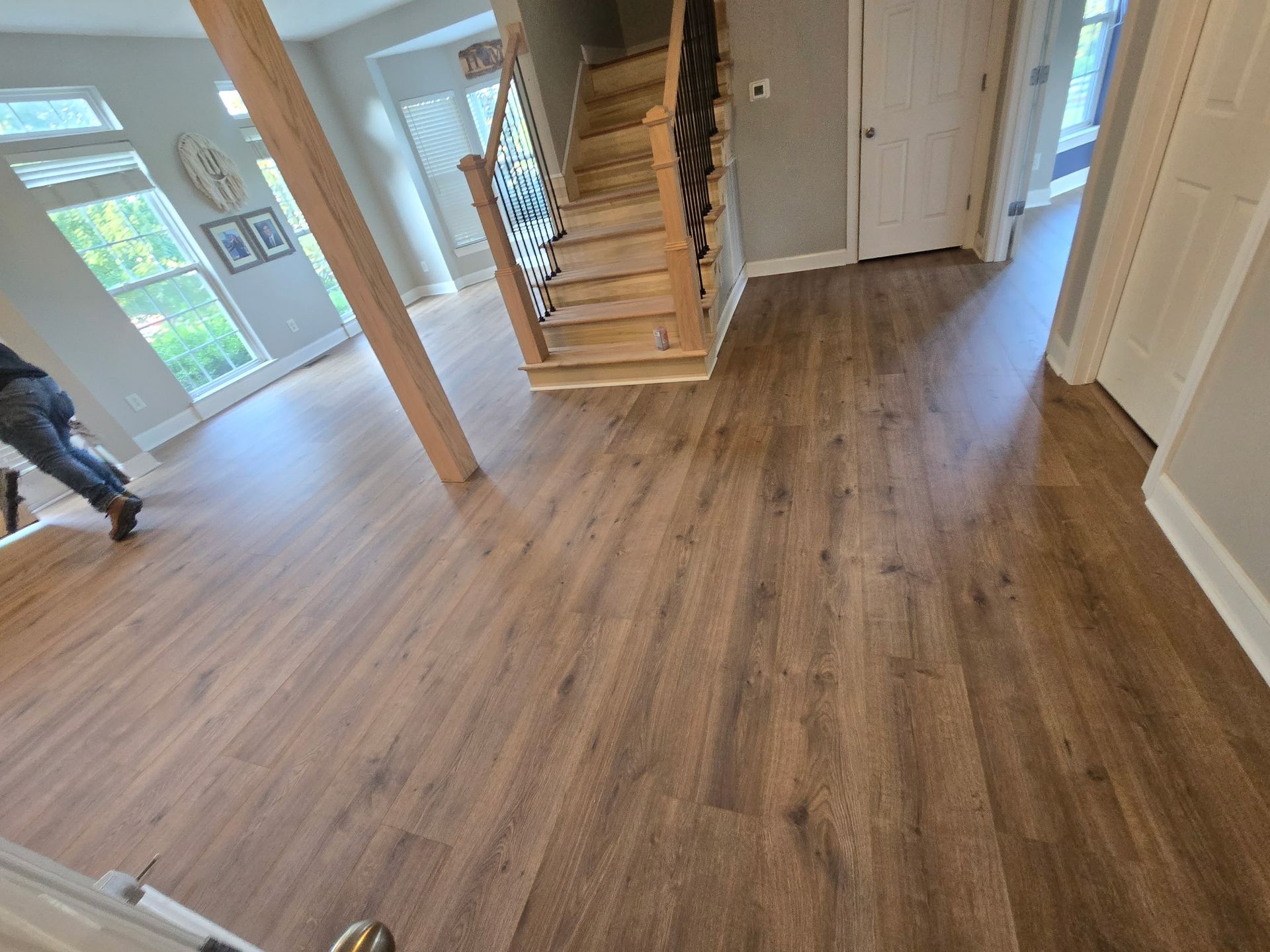 Wooden floor in a house with a staircase, a support beam, and a person walking.