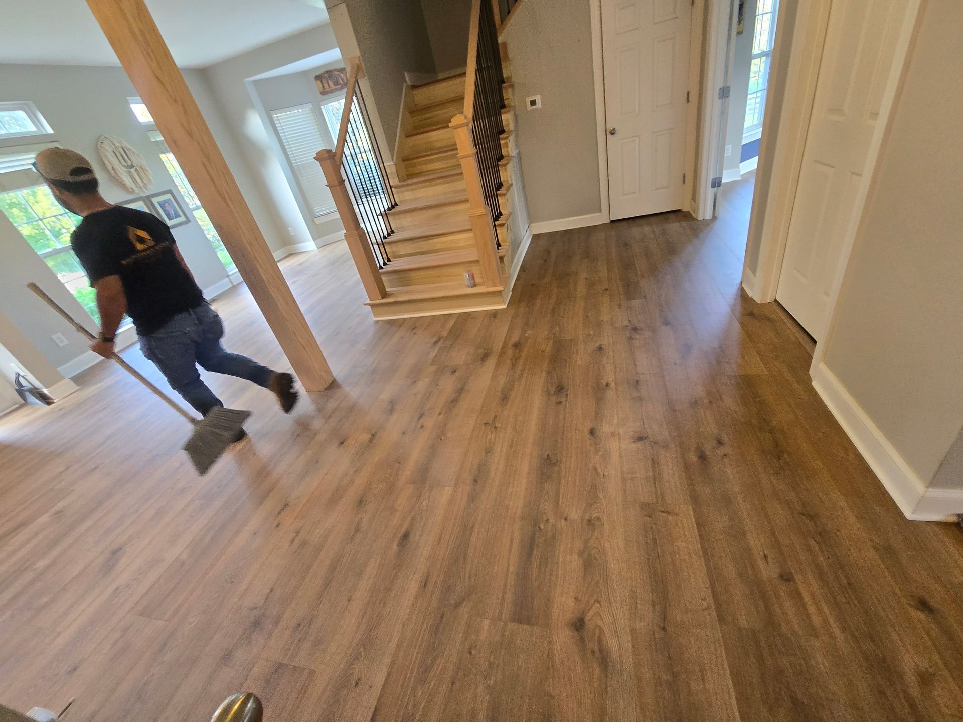 Man sweeping hardwood floor; stairs and door in the background.