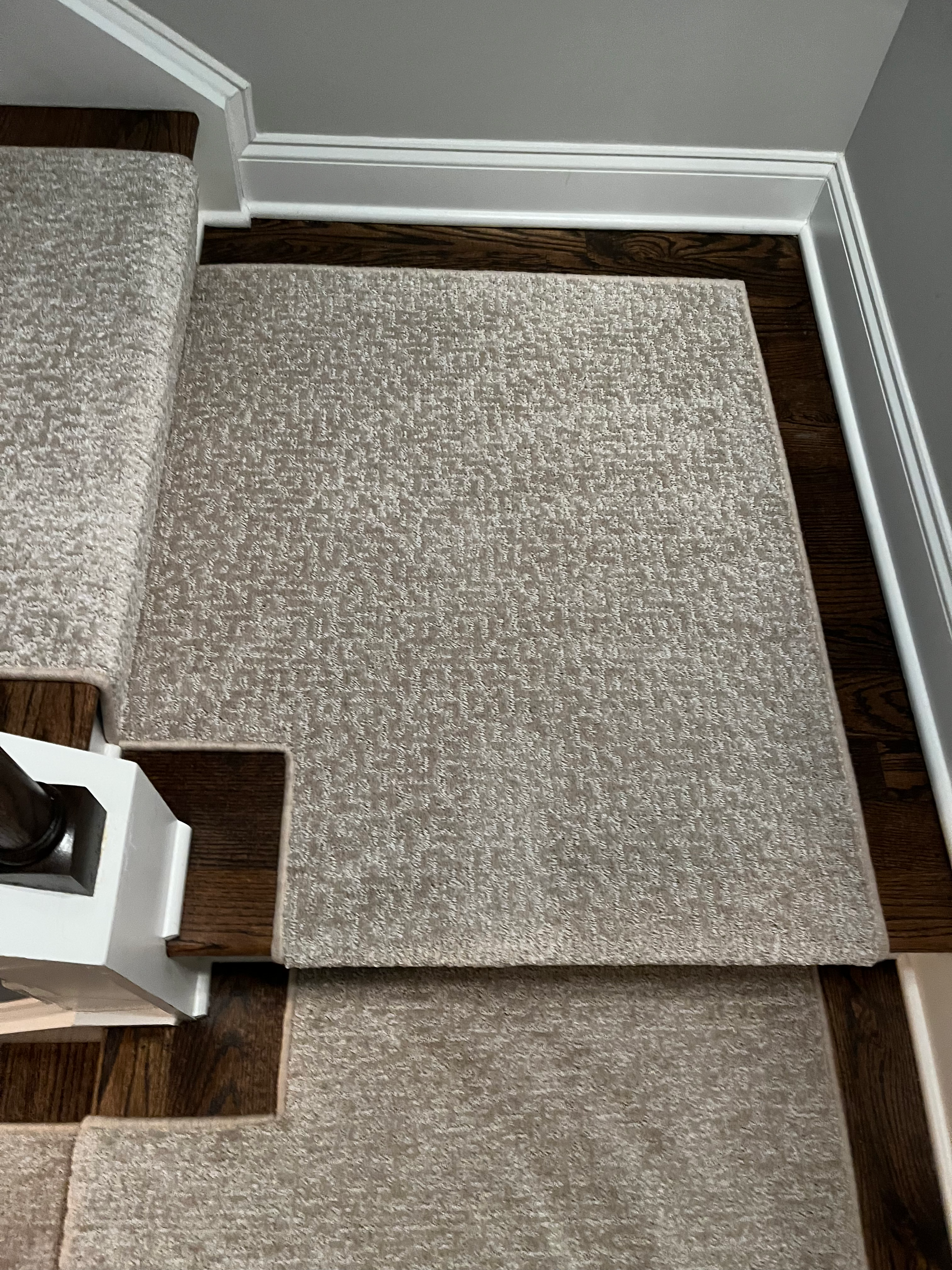 Staircase with carpet runner in shades of gray. Dark wood steps and white trim.