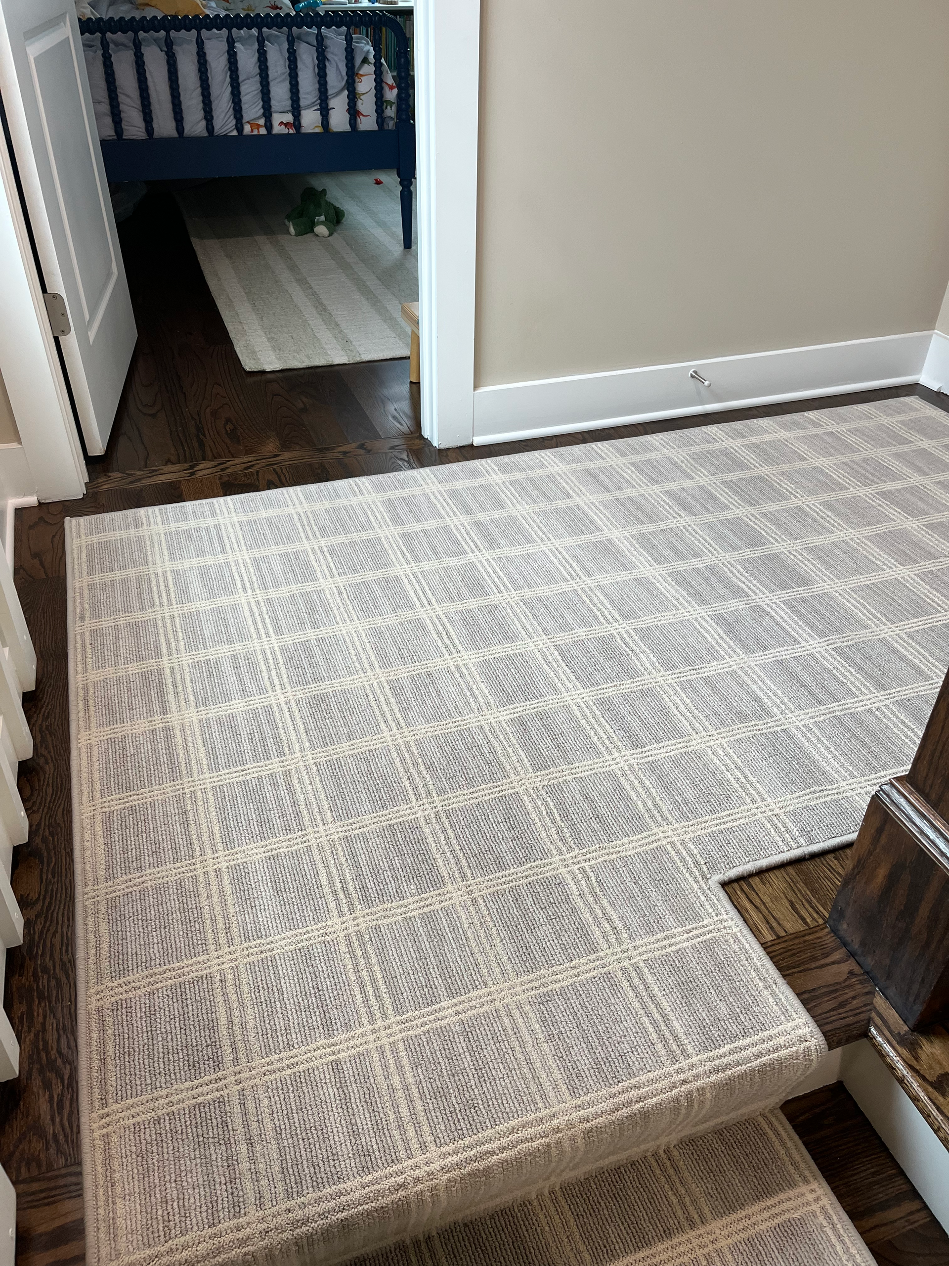 Staircase with gray and white patterned carpet and dark wood flooring, leading to a doorway.