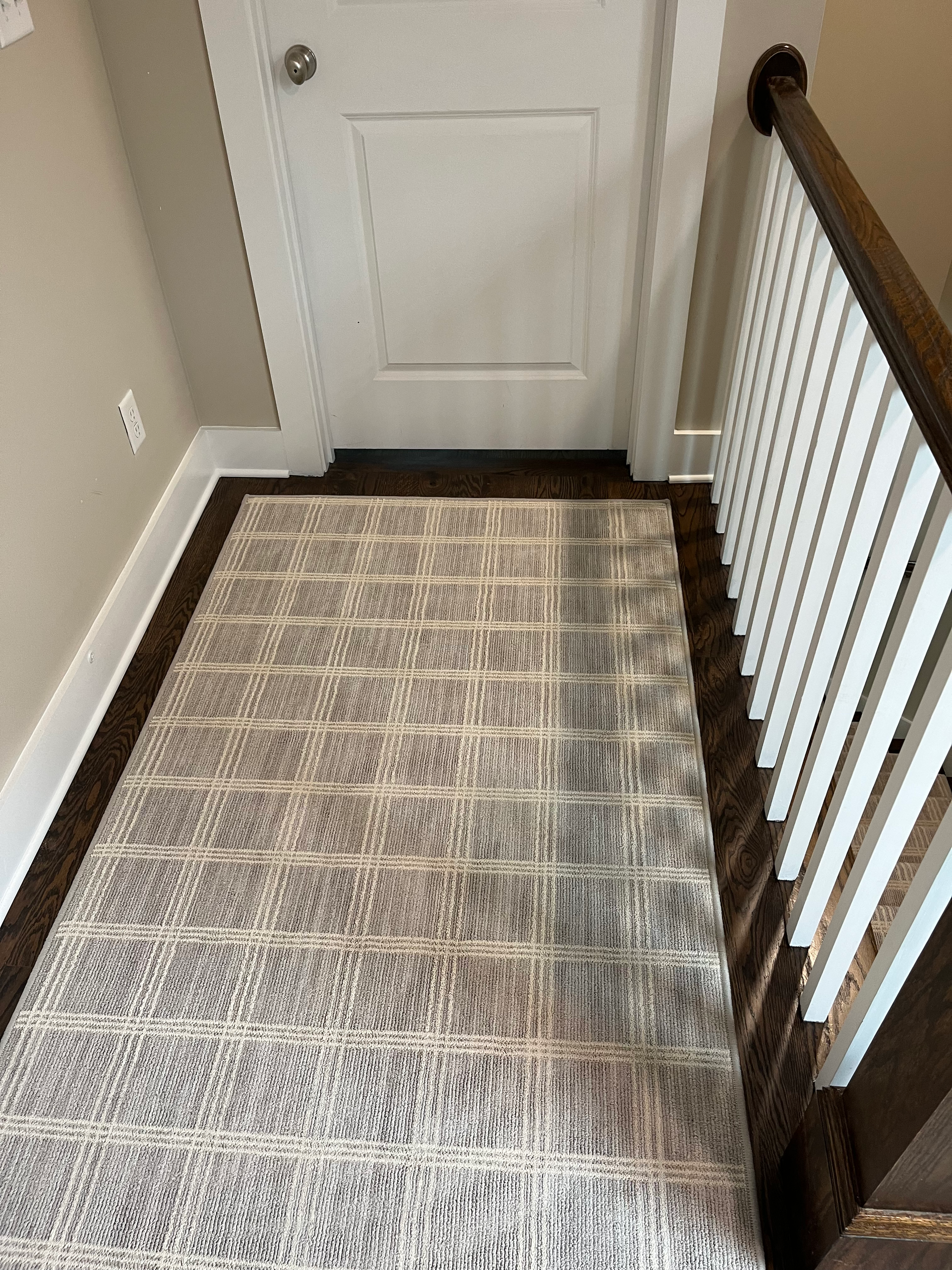 Area rug on dark wood floor in front of a closed white door near a staircase.