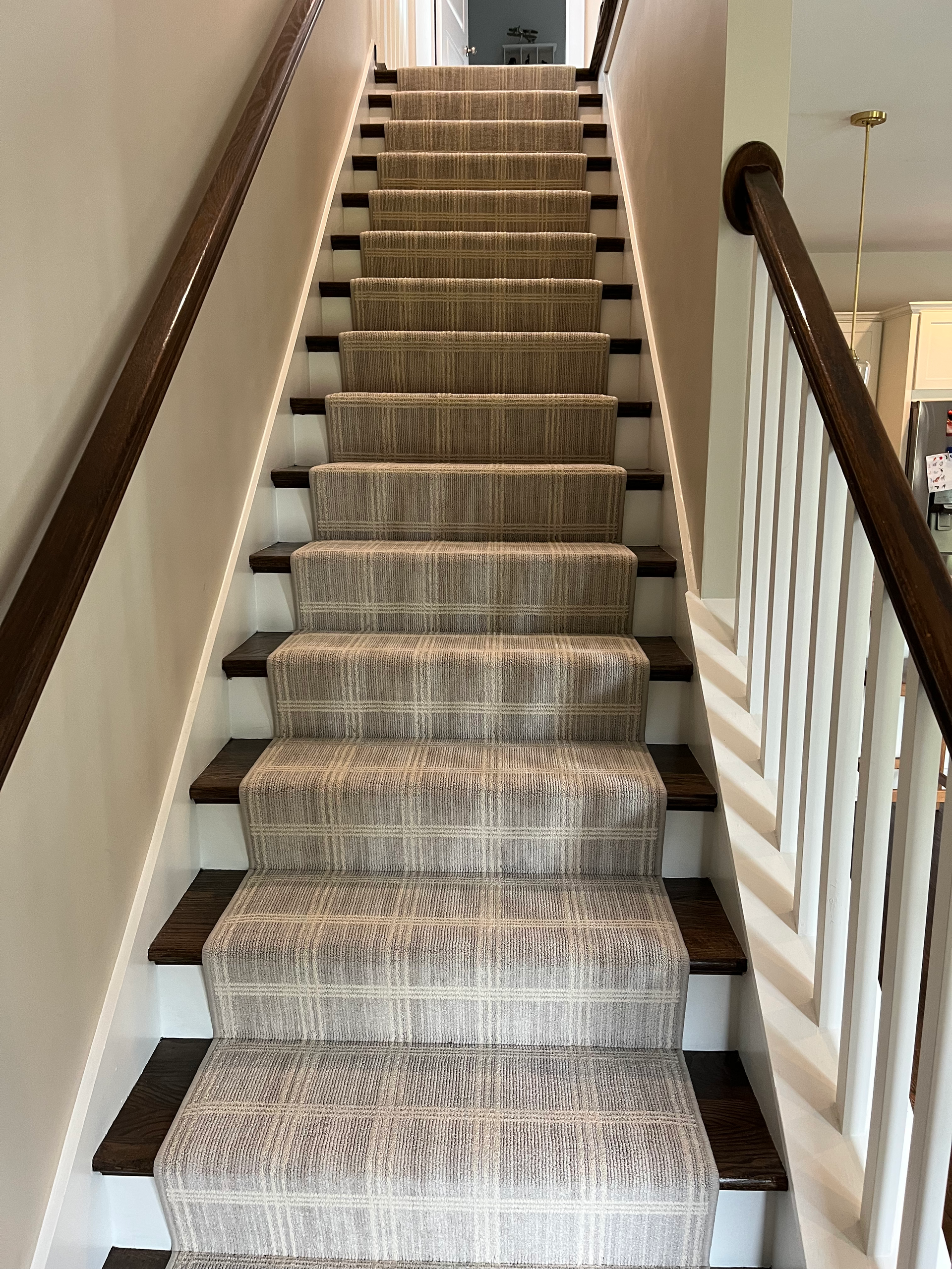 Staircase with neutral carpet runner, dark wood treads and handrails, and white banister.