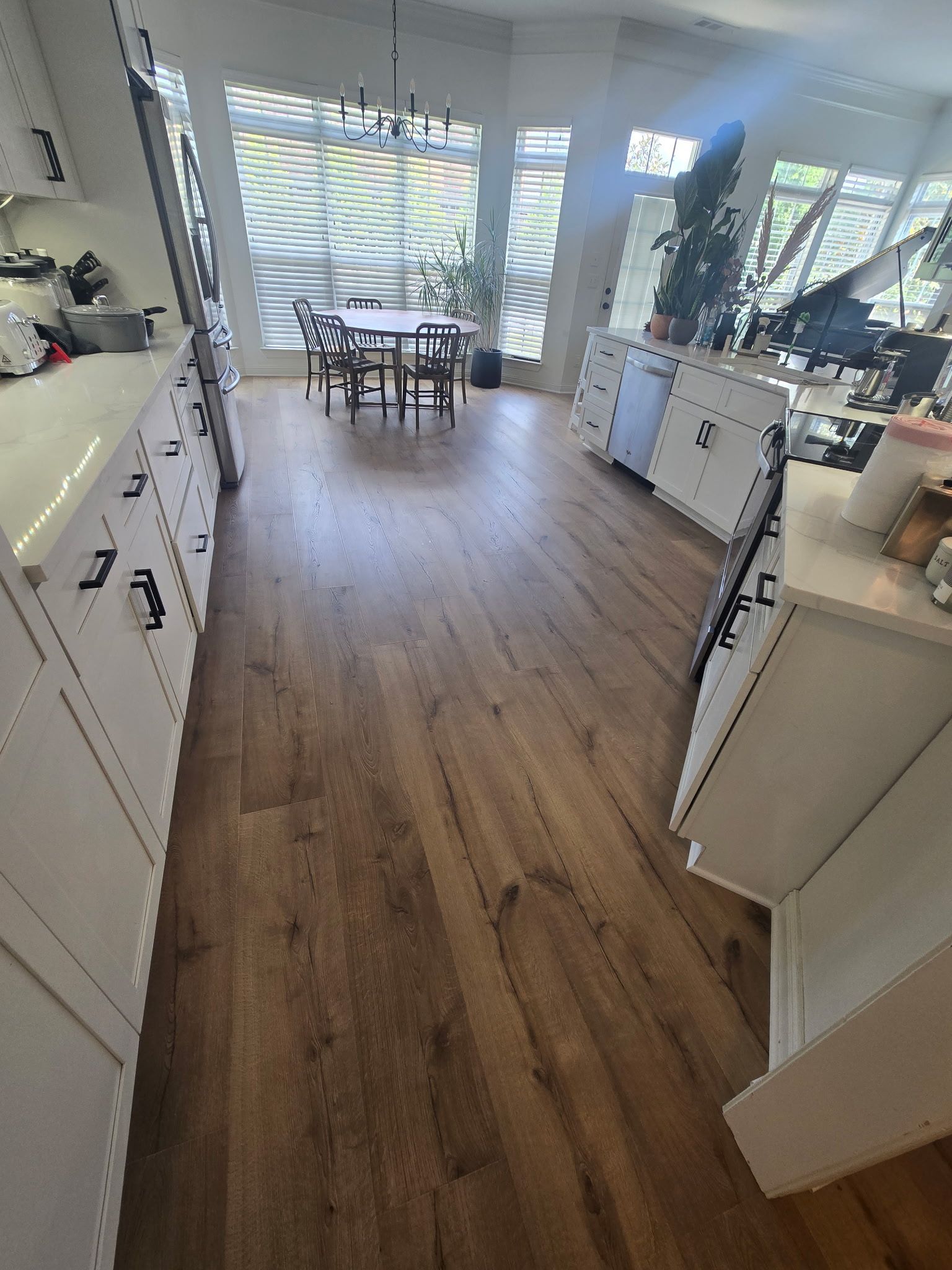 Kitchen with wood-look floor, white cabinets, and a dining table near a window with blinds.