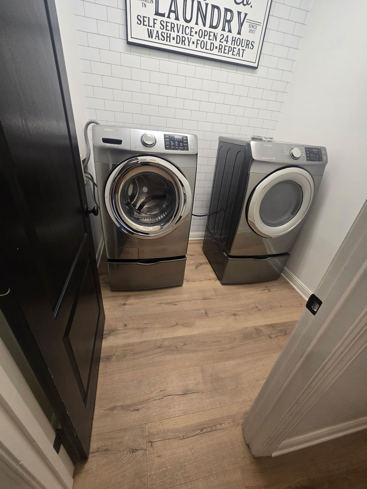 Laundry room with silver washer and dryer, wood floor, and patterned wallpaper.