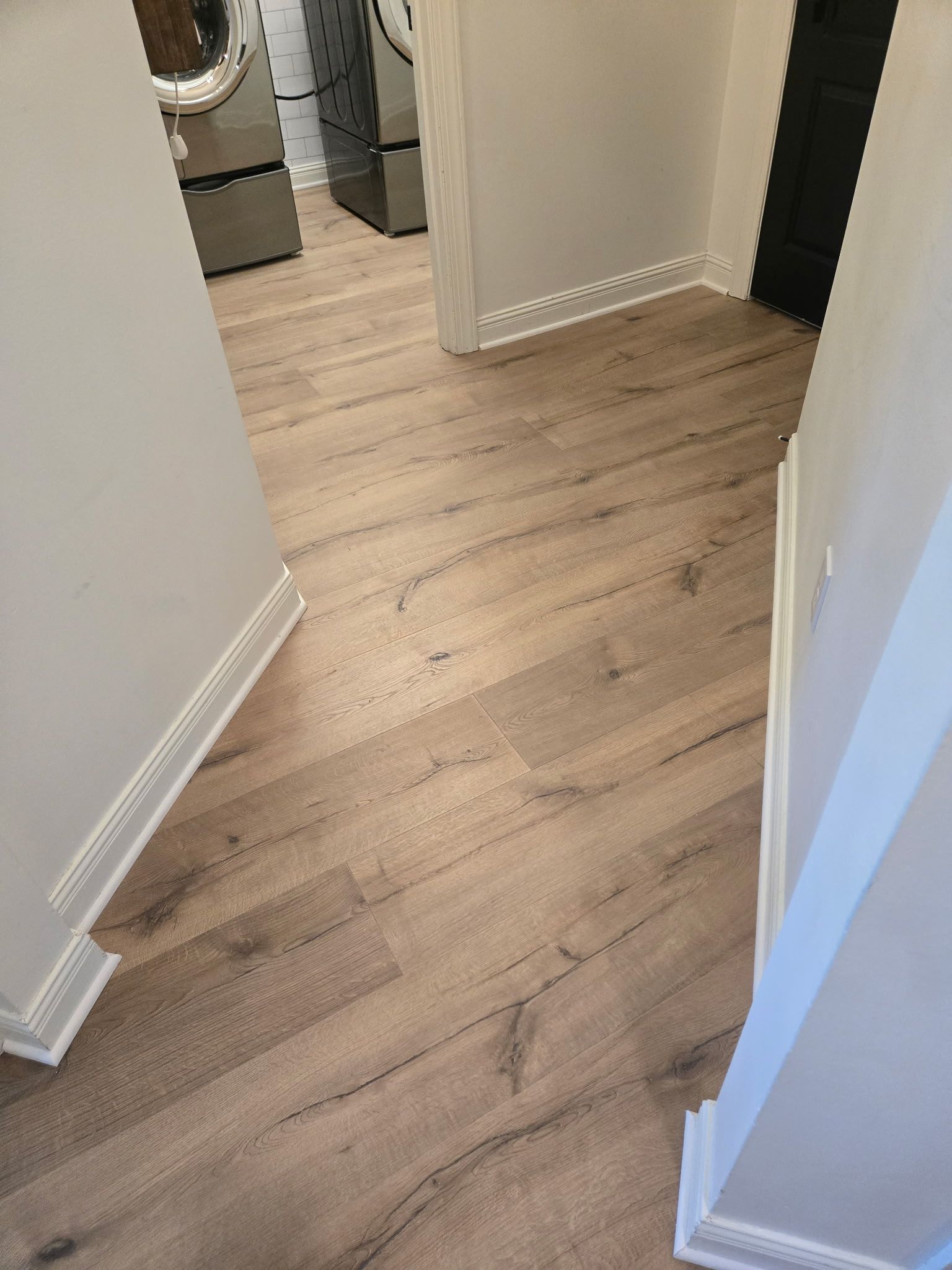 Hallway with wood-look flooring, white walls, and trim. A black door is visible at the end.