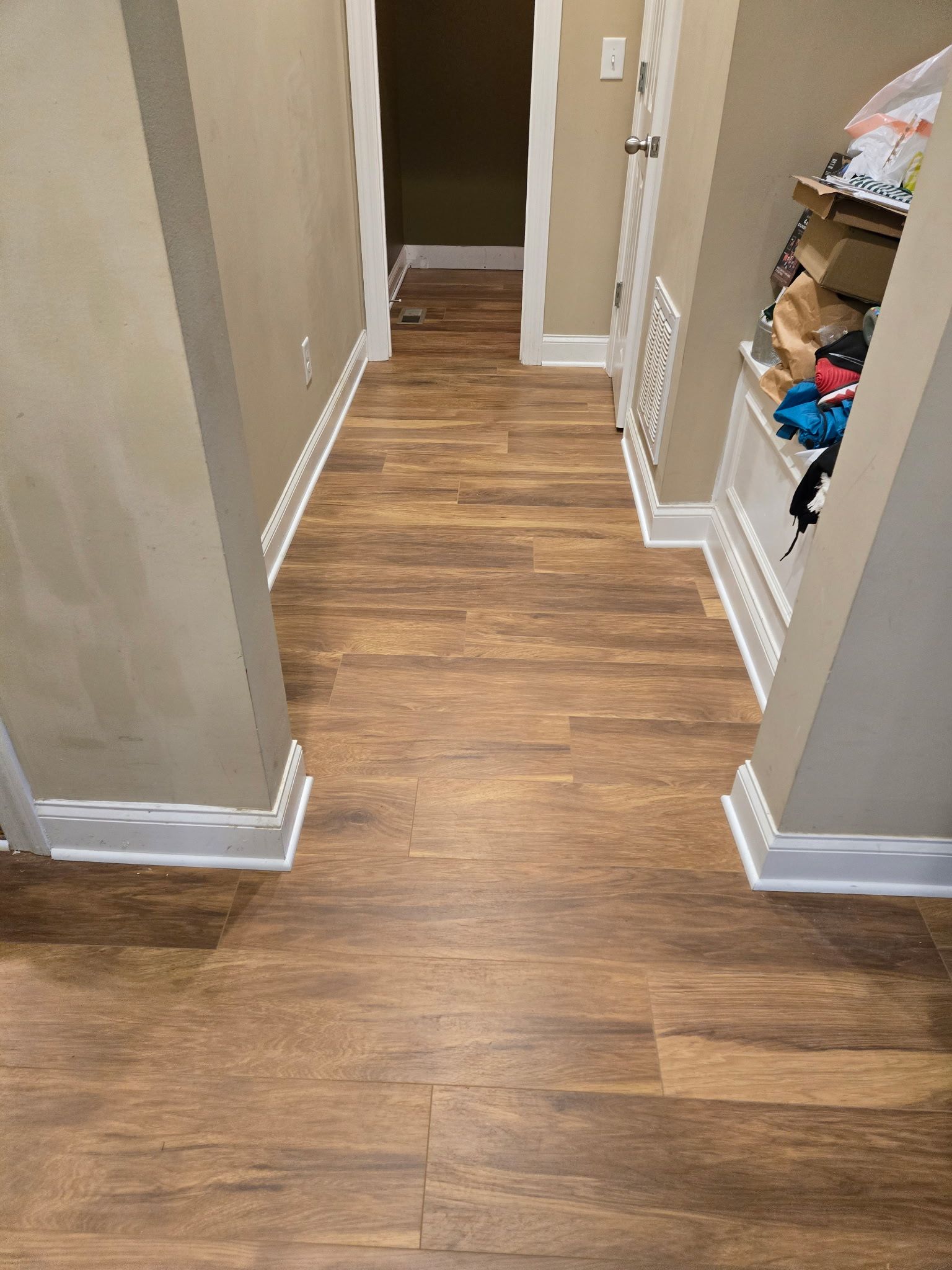 Hallway with wood-look flooring, white trim, and tan walls. A built-in shelf is on the right.