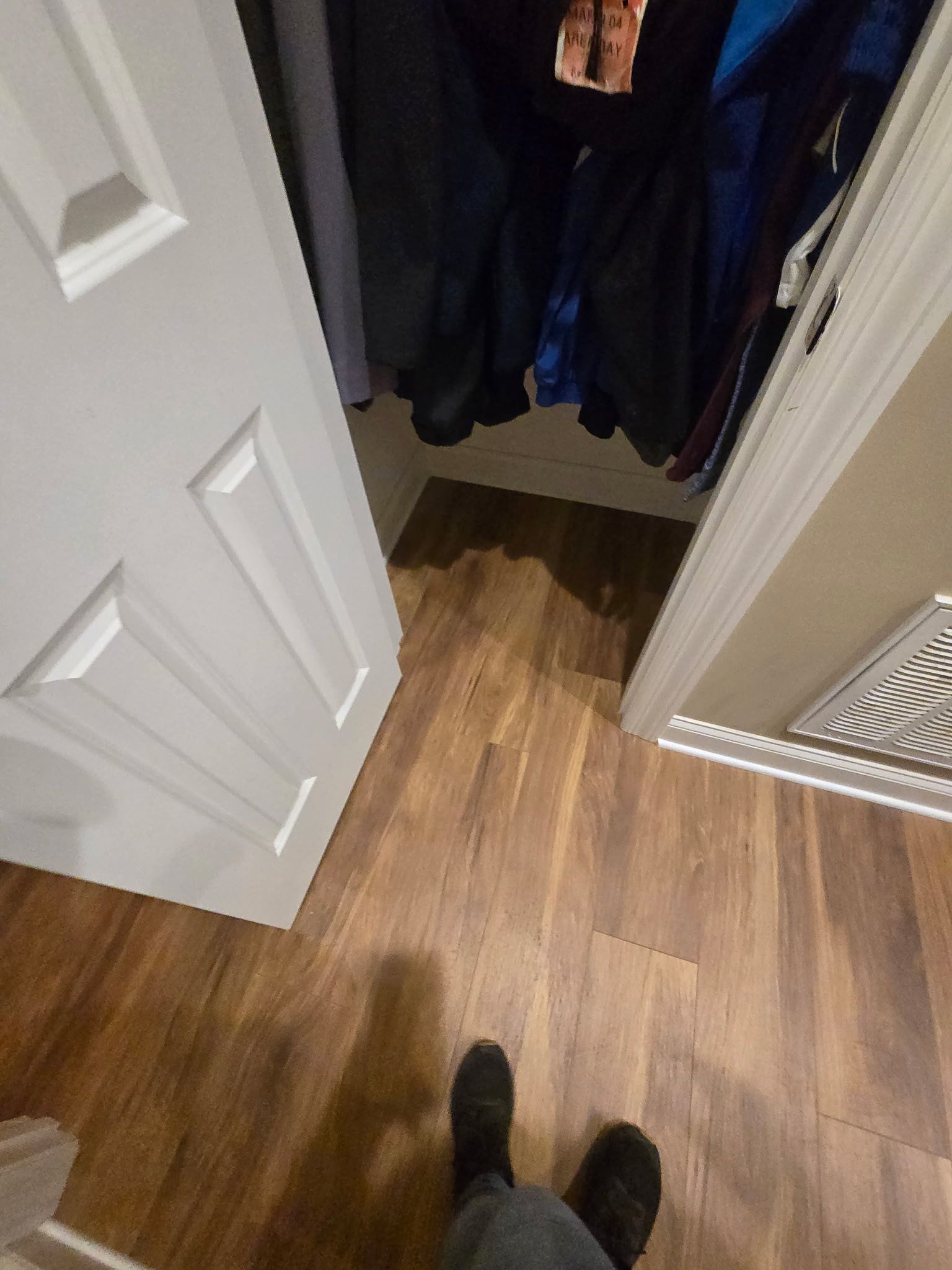 Person standing in front of an open closet. Brown wood flooring, white door, clothes hanging inside.