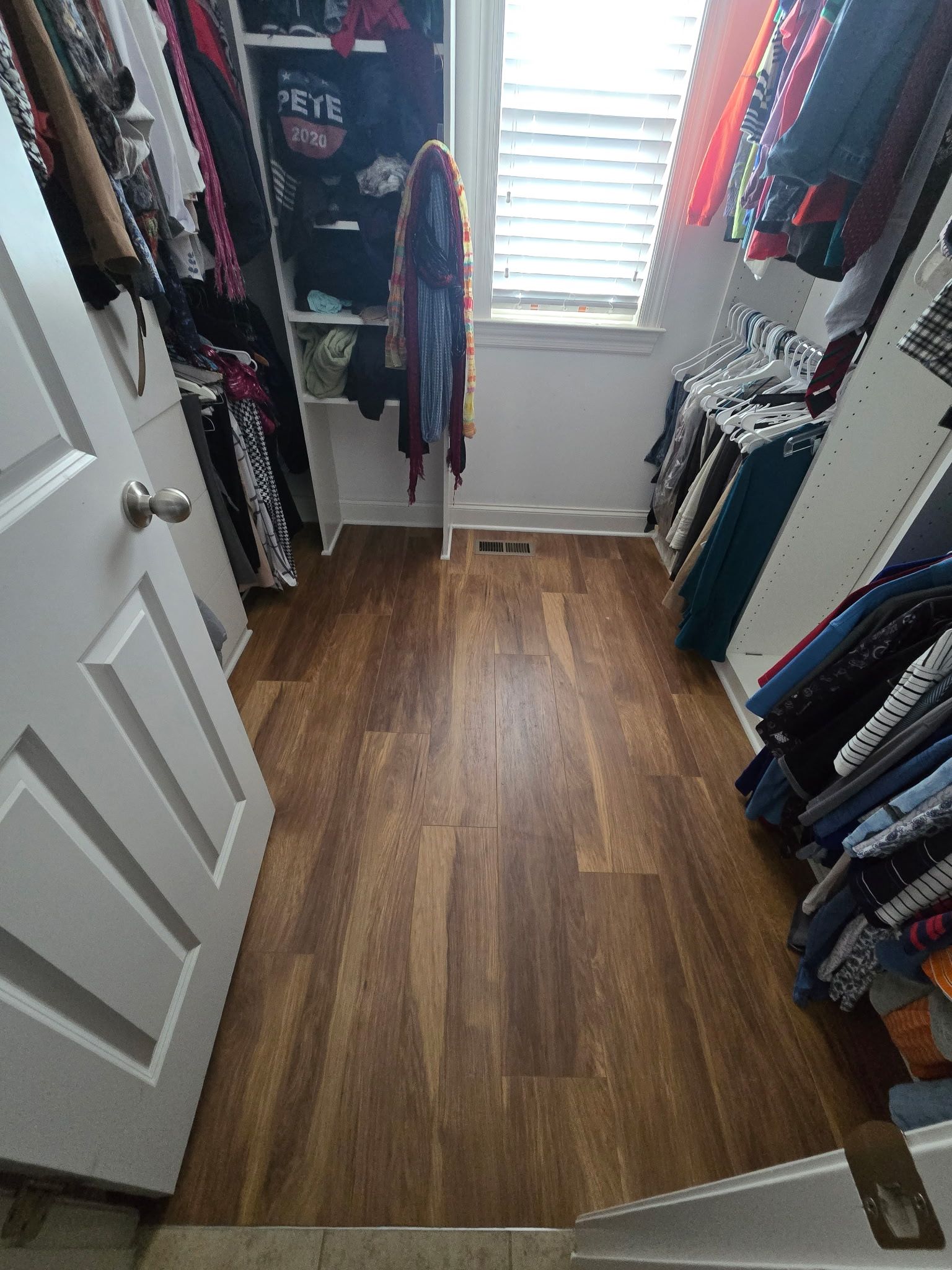 Closet with wooden floor, clothes racks on both sides, and a window in the back.