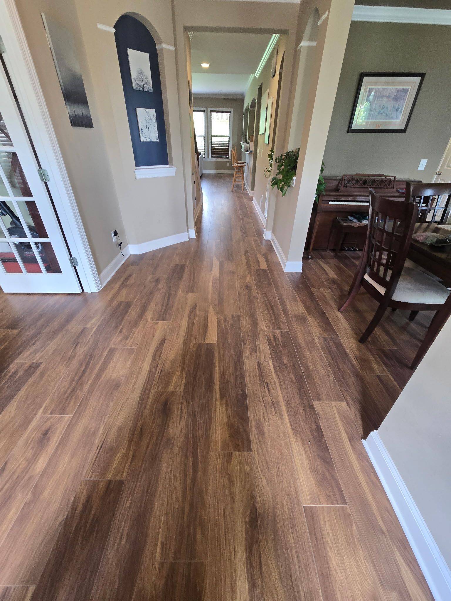Wooden floor hallway with archway and art, leading to distant window.