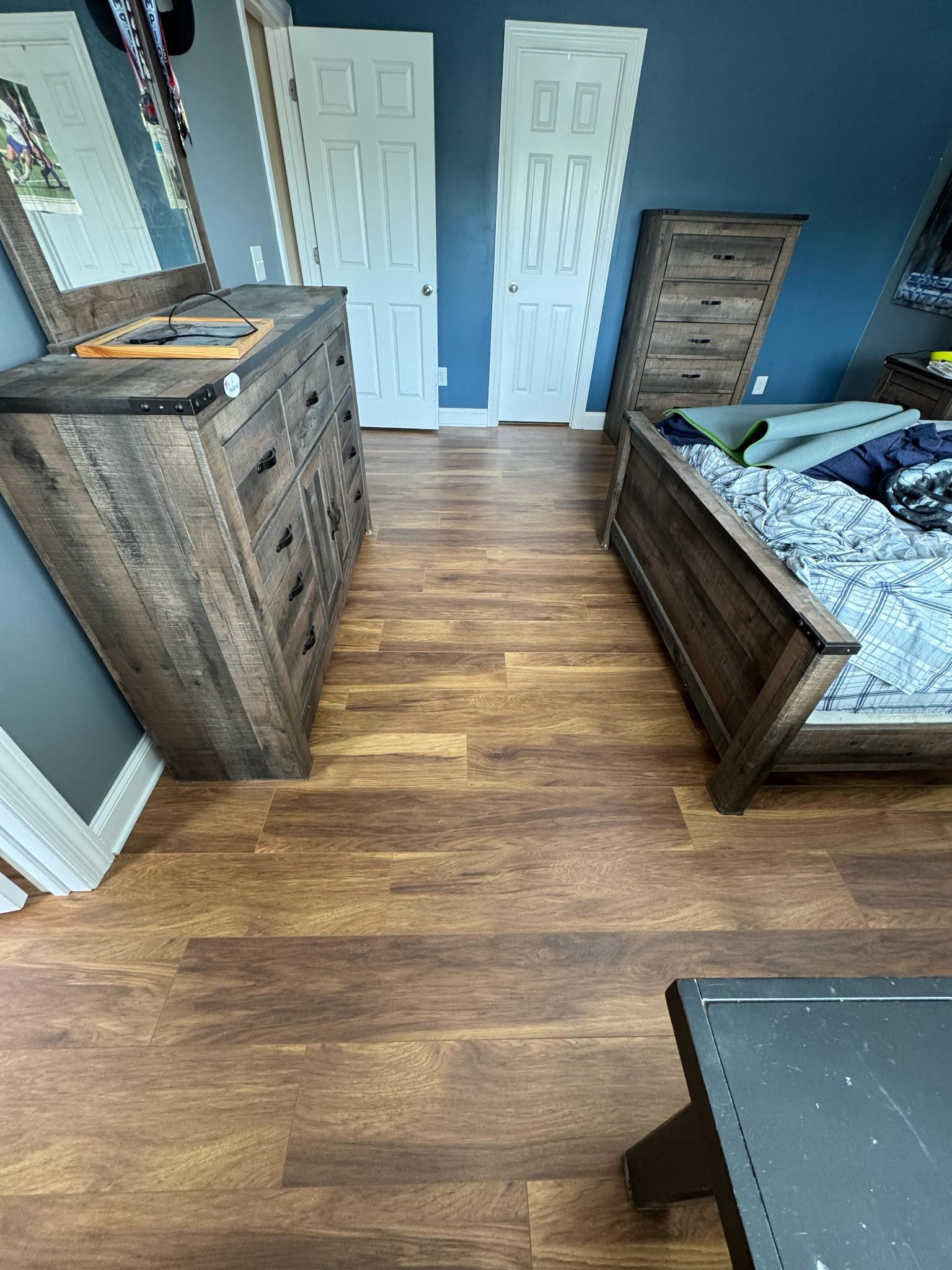 Bedroom with wooden furniture on wood-look flooring, including a dresser and bed against blue walls.