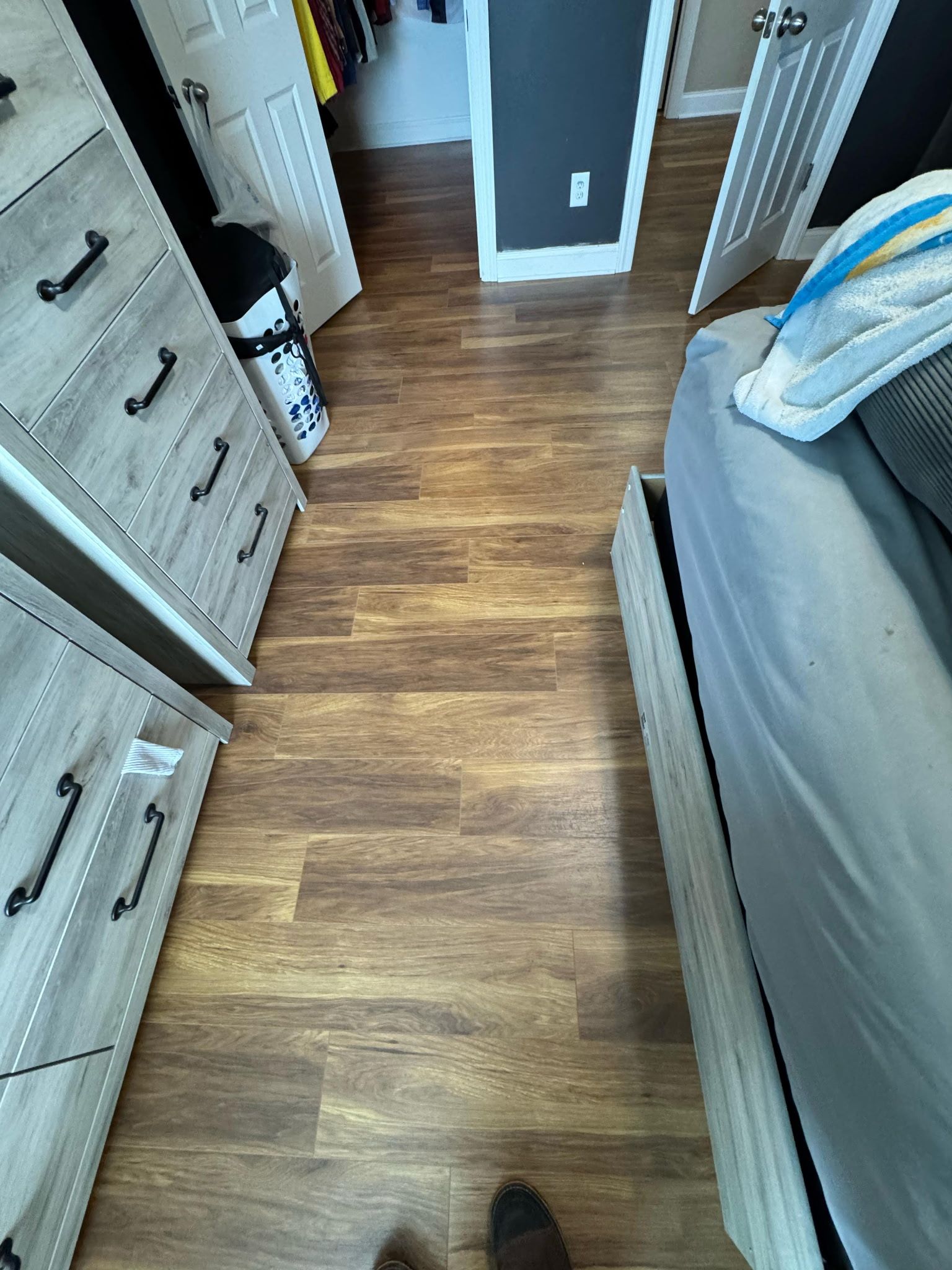 Bedroom with wood-look flooring, dressers on the left, bed on the right, and doors in the background.