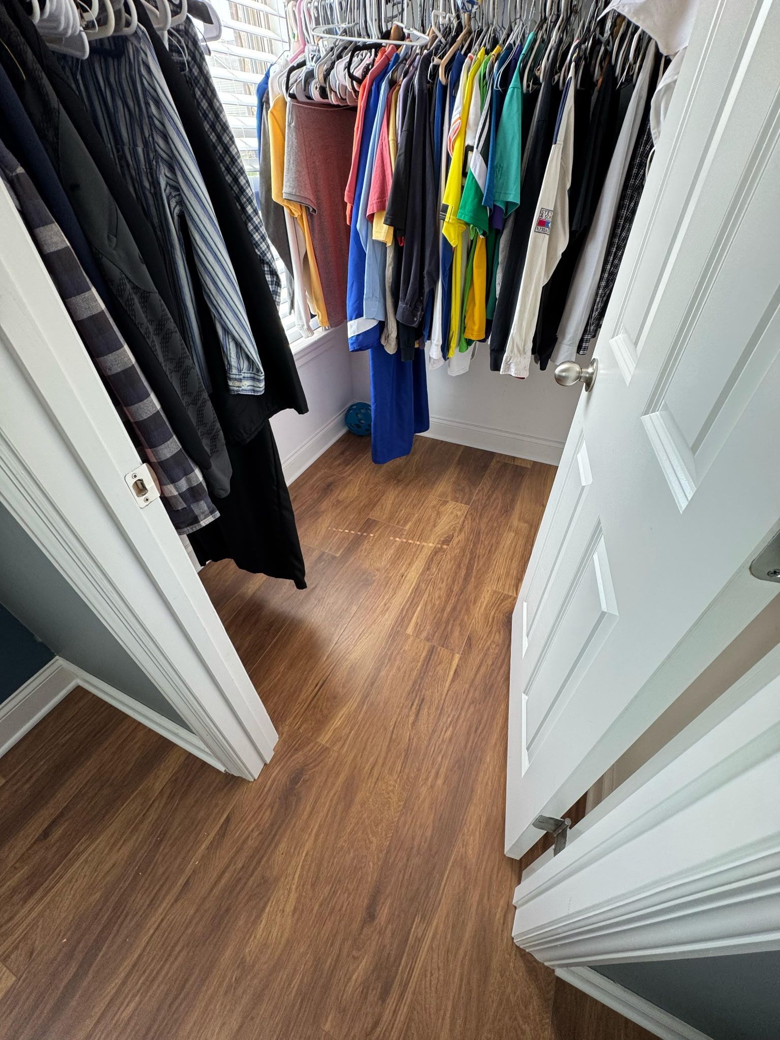 Walk-in closet with wood-look floor, clothes on racks, and white doors.