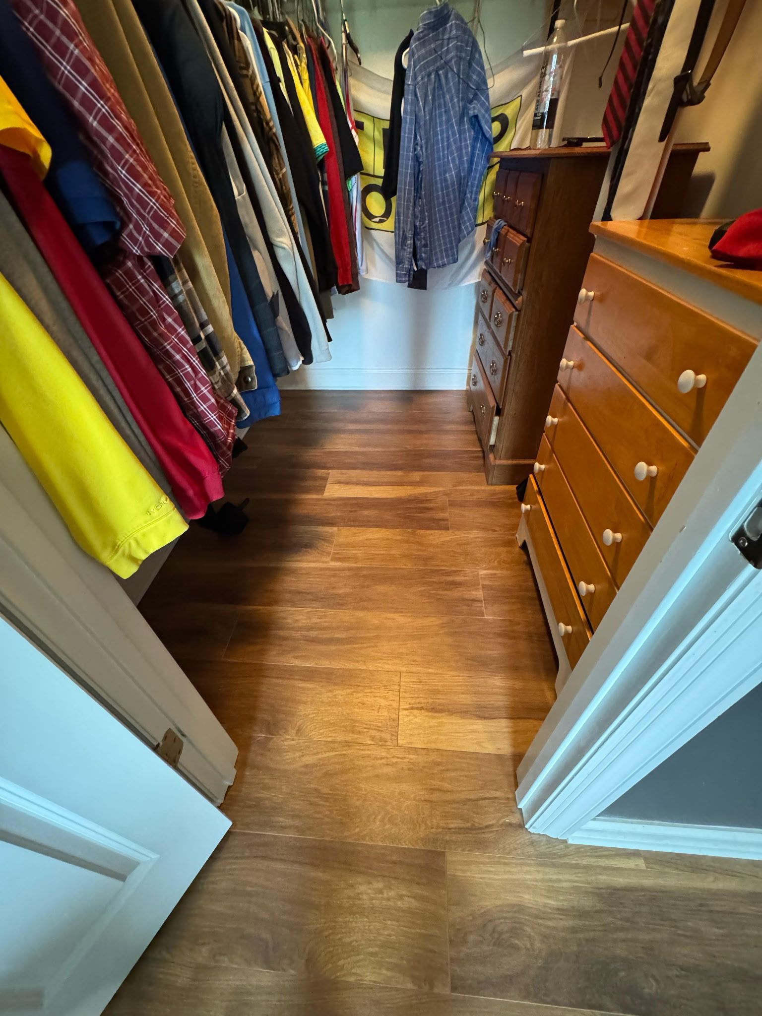 Walk-in closet with hardwood-style floor. Clothing racks on left and chest of drawers on right.