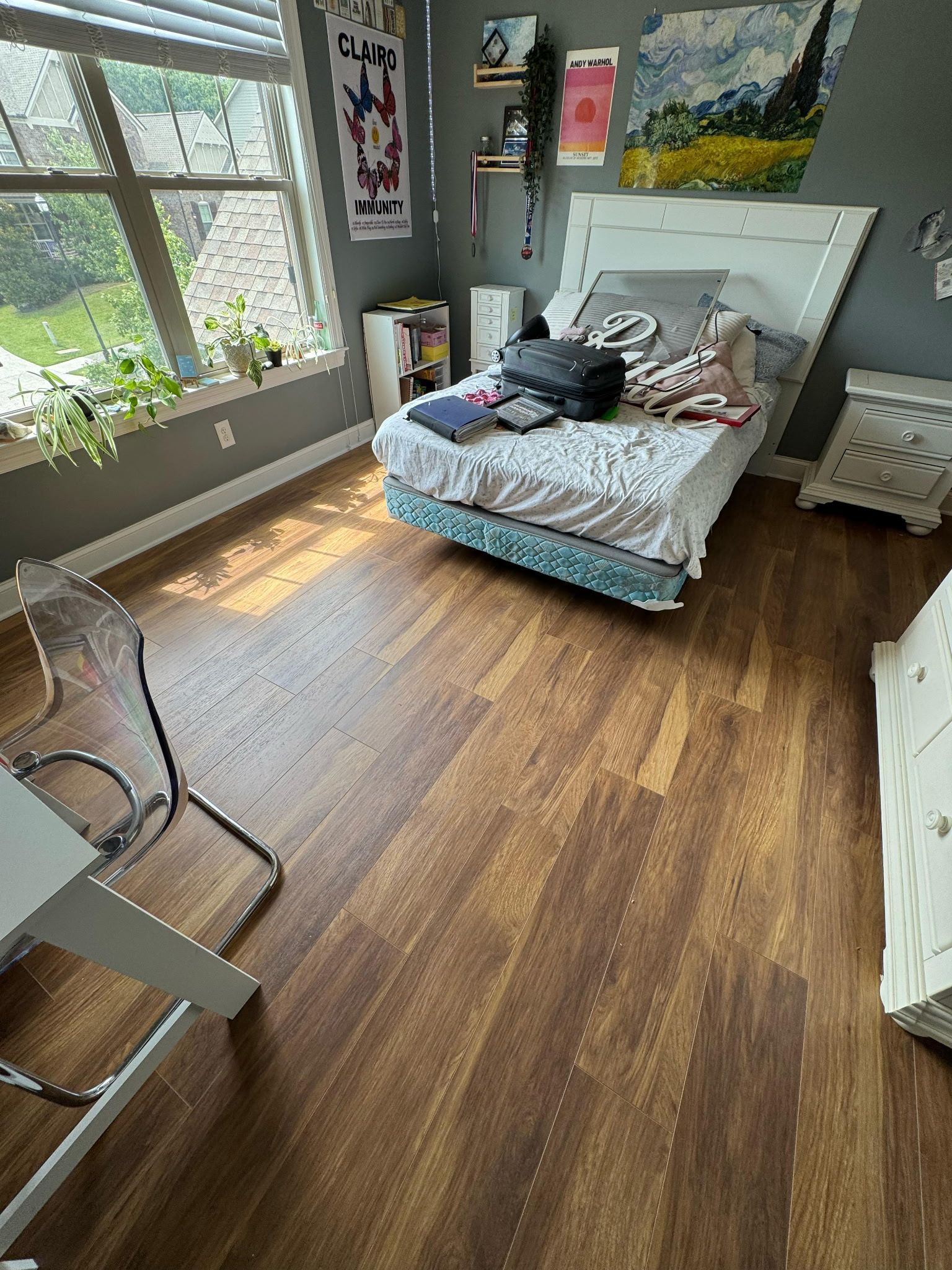 Bedroom with wood-look floors, bed, window, desk, and gray walls.