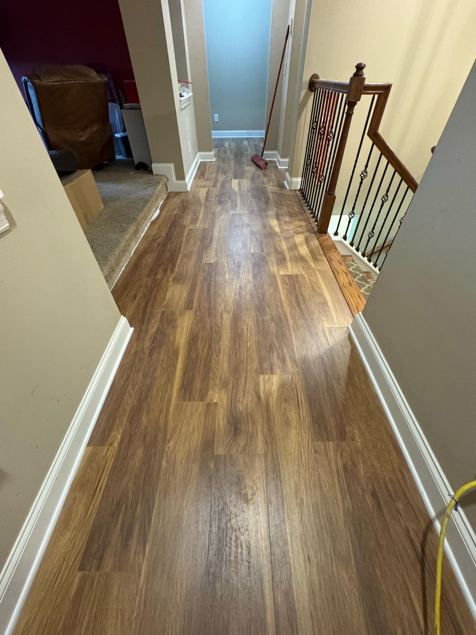 Long hallway with wood-look flooring. Staircase on the right, a red wall and carpet on the left.