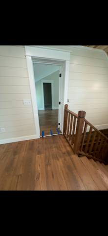 Interior view of a room with wood flooring, a doorway, and wooden stairs. White walls and trim.