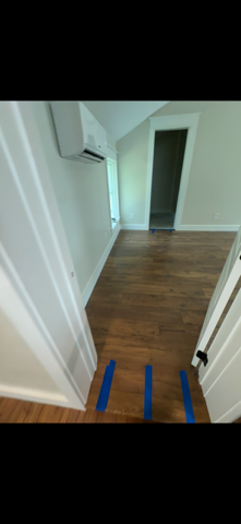 A room with wooden floor, white walls and trim, and a wall-mounted air conditioner. Blue tape lines the doorway.