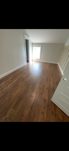 Empty room with wood flooring, light-colored walls, and a window letting in bright light.