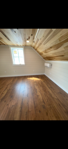 Cozy attic room with wood ceiling, window, wood floor, and white walls.