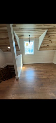 Interior of a room with wood floors, white walls, and a wood-paneled ceiling.