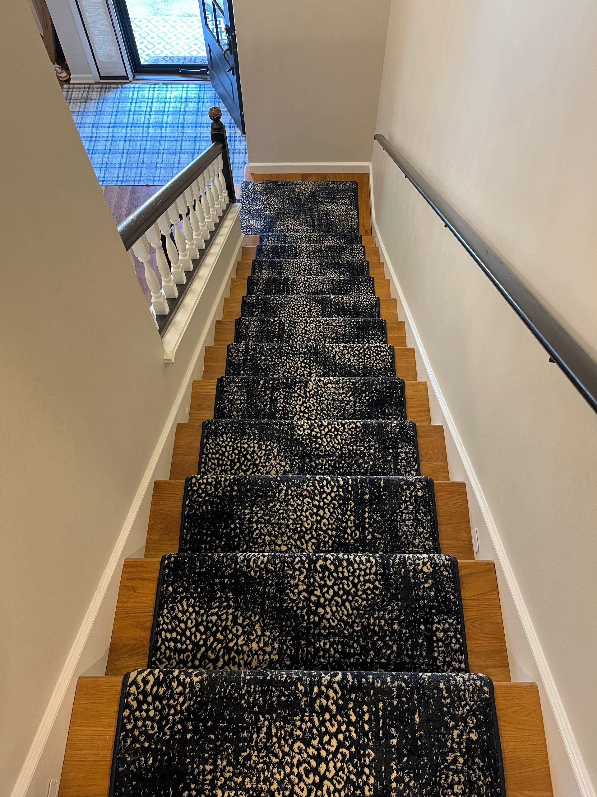 Staircase with patterned black and cream runner, wooden steps, white trim, and a dark railing.