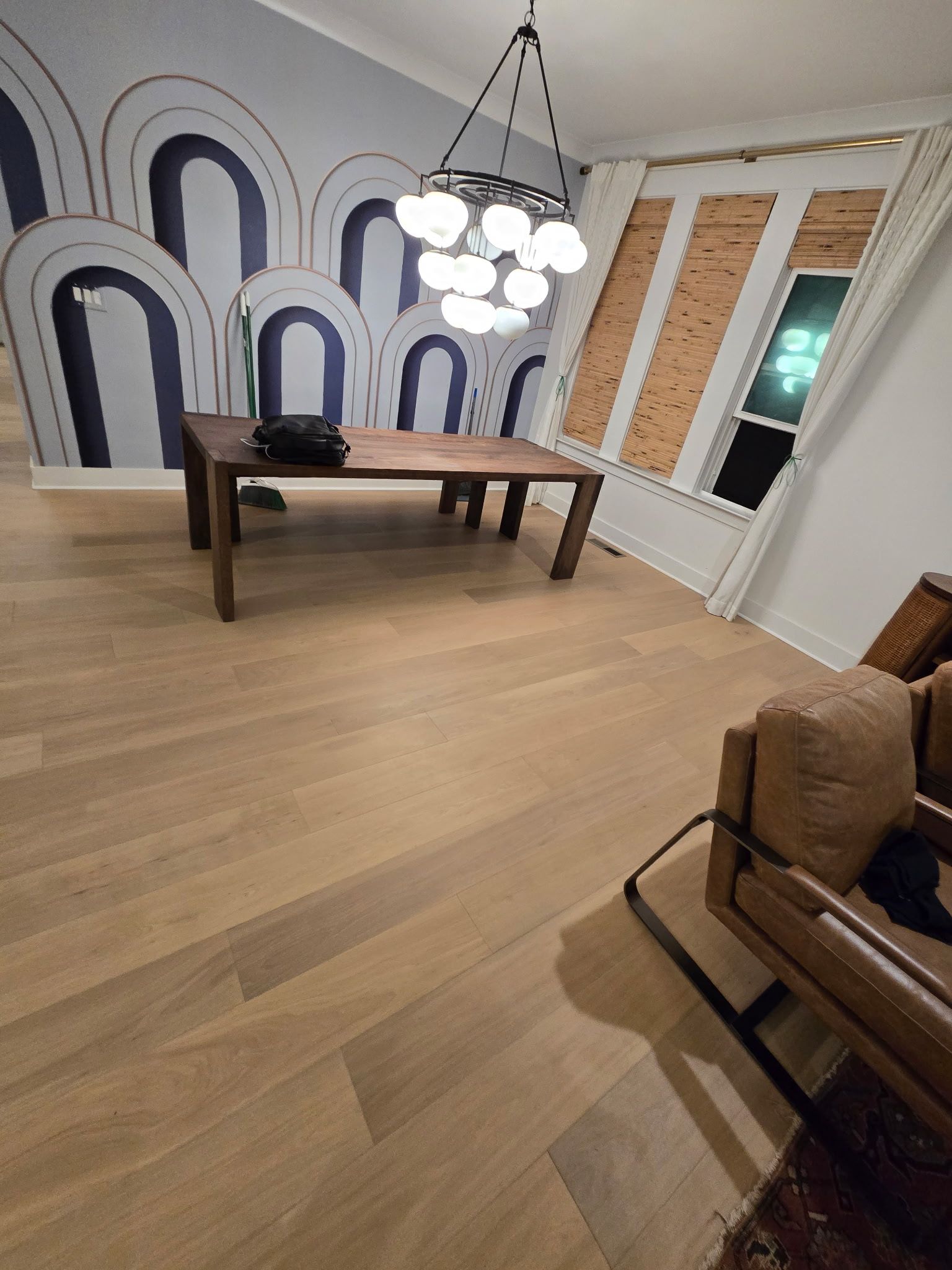 Wooden dining table in a room with hardwood floors and a decorative wall, lit by a modern chandelier.