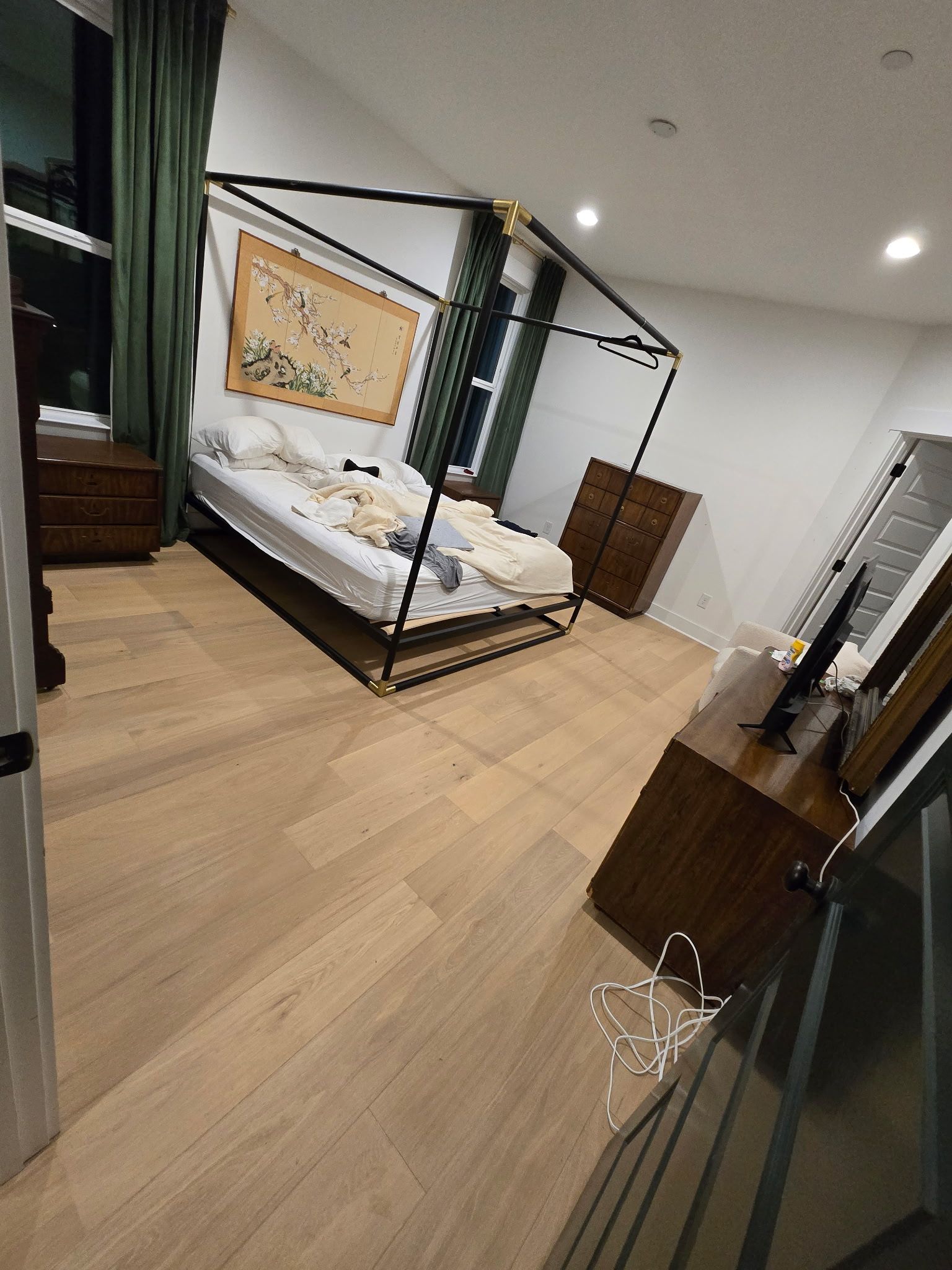 Bedroom with a canopy bed, dresser, and wood floors.
