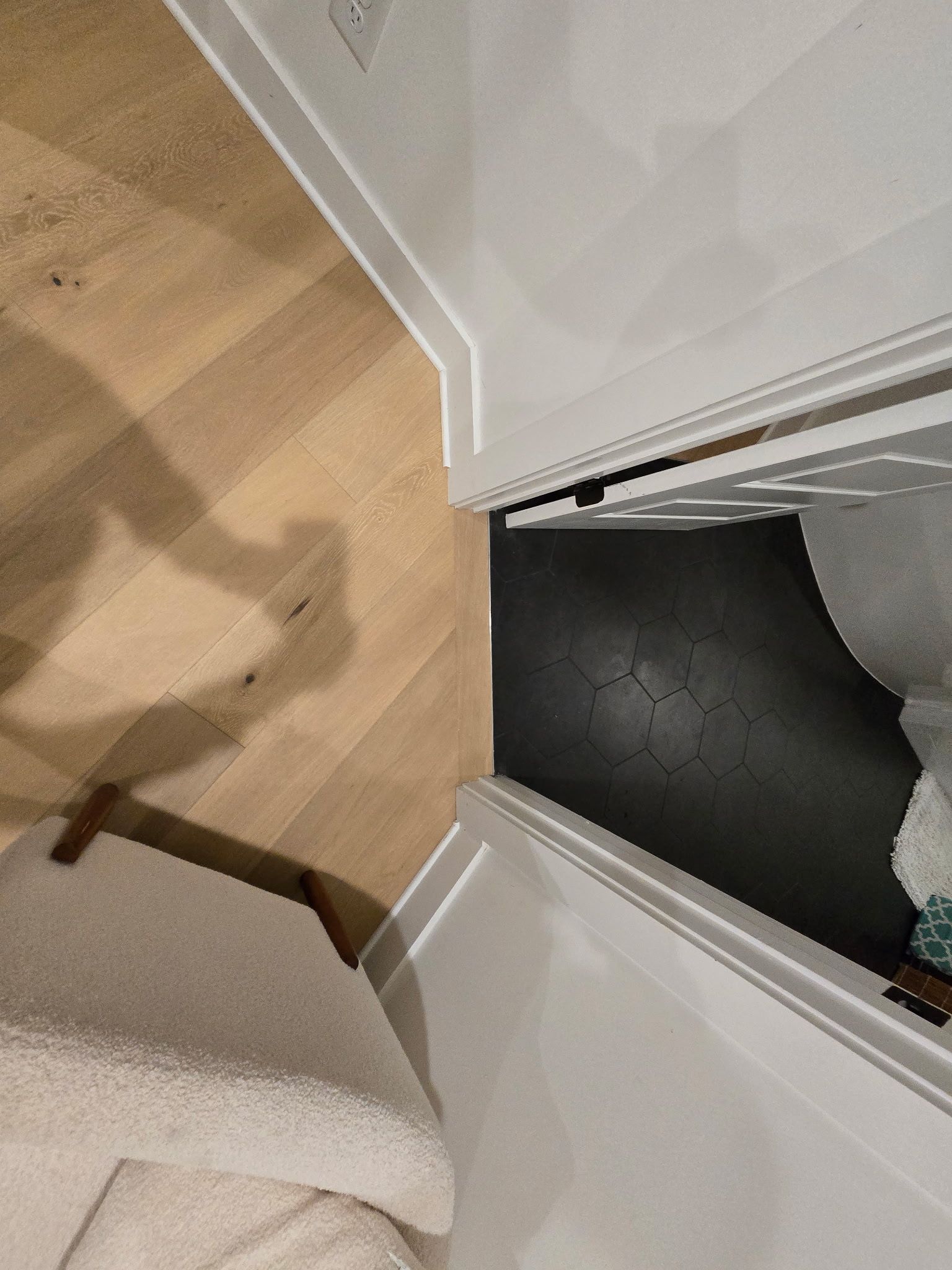 Light wood floor leads into a doorway with dark flooring, white trim, and a chair.