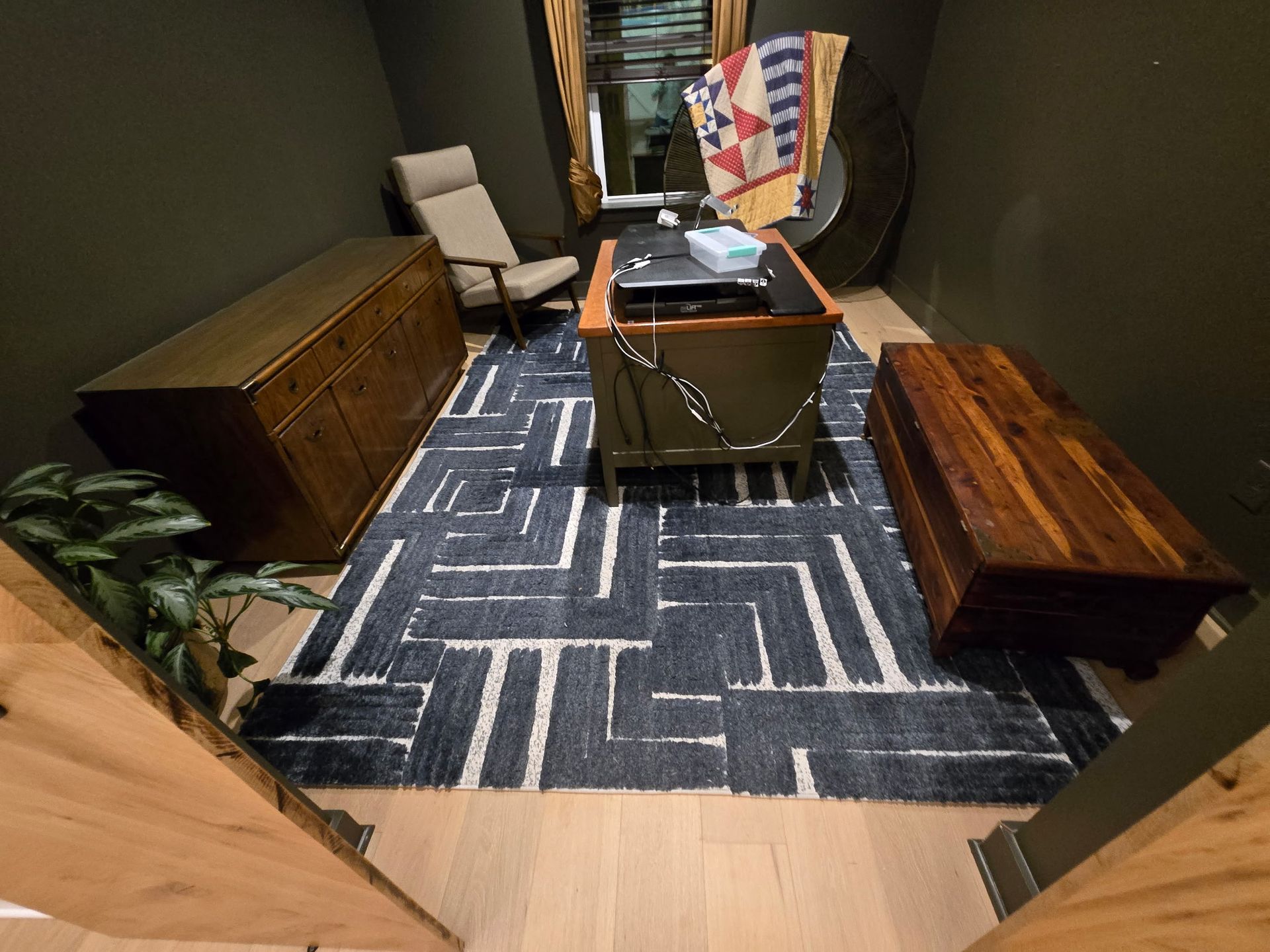 Cozy, dark-walled office with wood furniture, patterned rug, and a window.