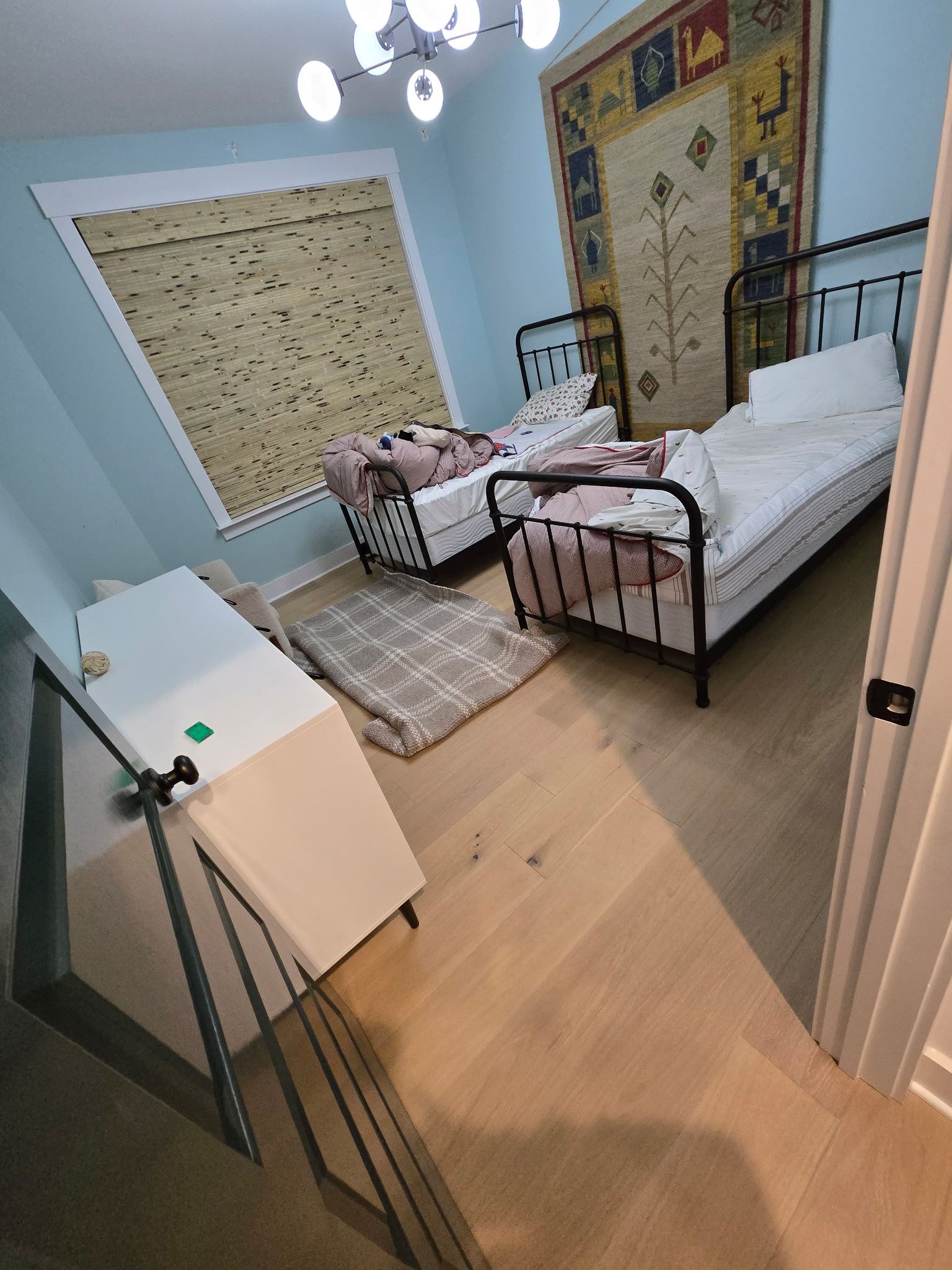 Bedroom with two beds, white dresser, wooden floor, and a large tapestry hanging on the wall.
