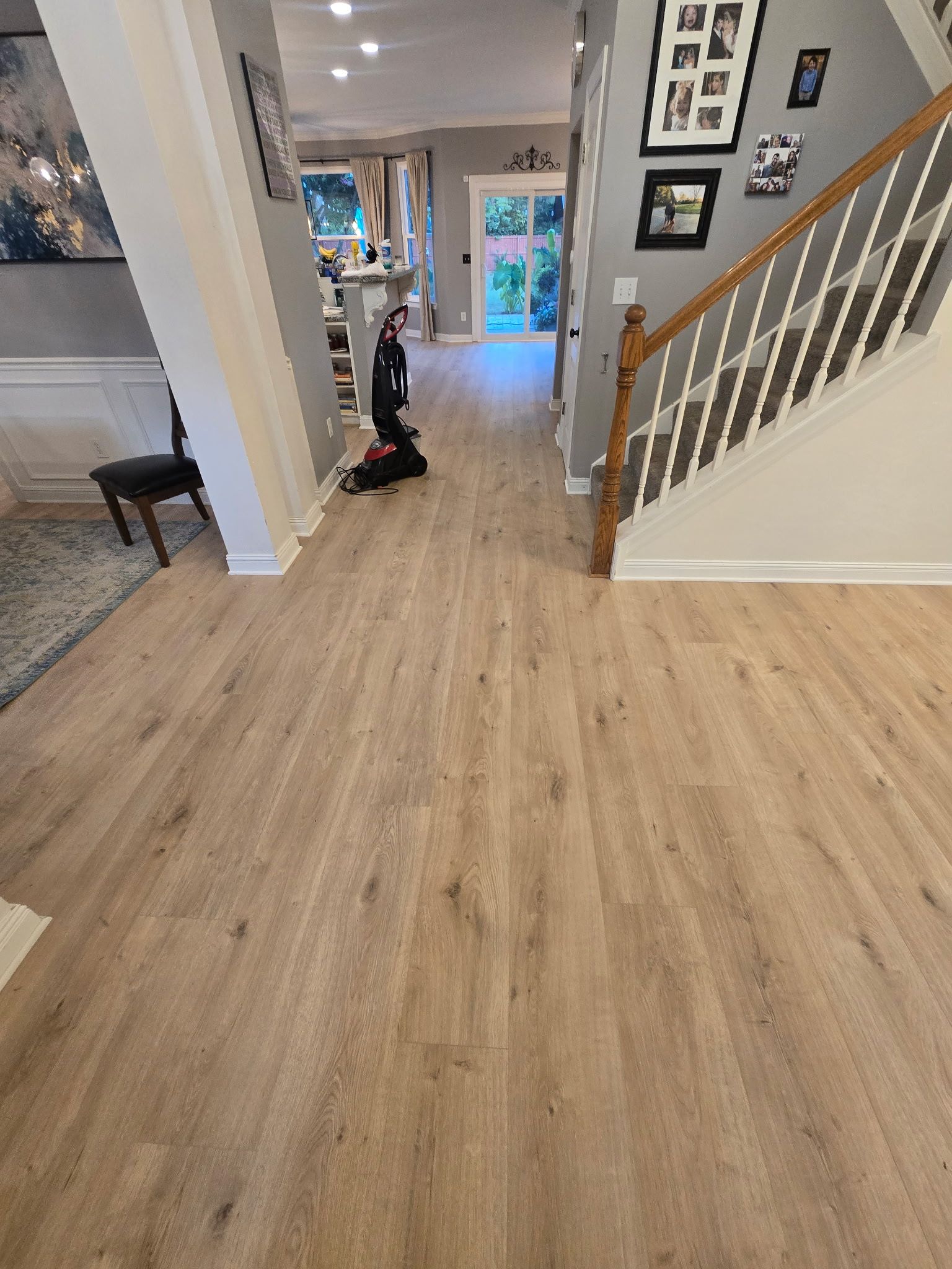 Entryway with wood-look flooring, leading to a back door. A staircase on the right and art on the left.