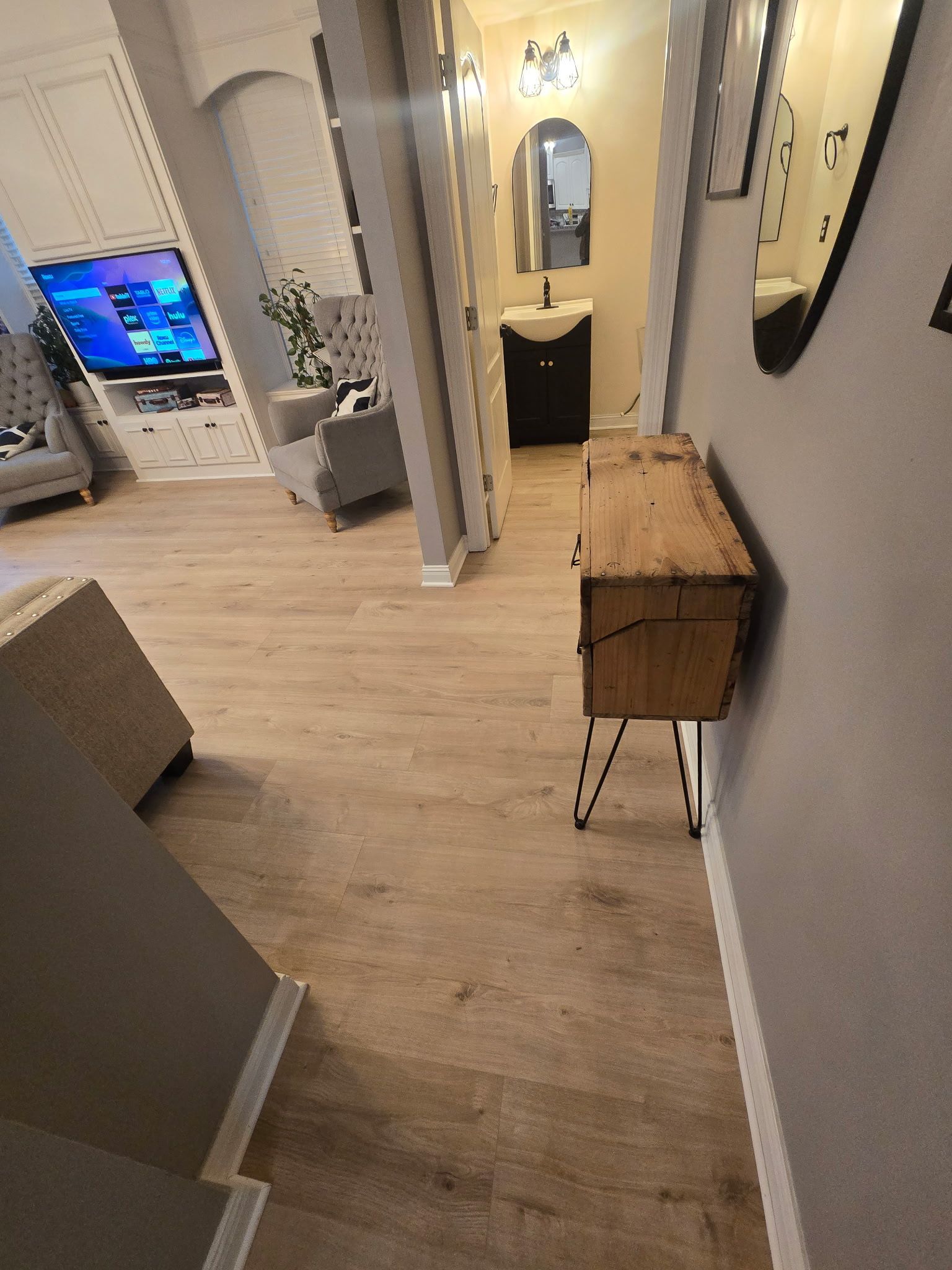 Hallway with wood console, leading to a bathroom with a black vanity and arched mirror.
