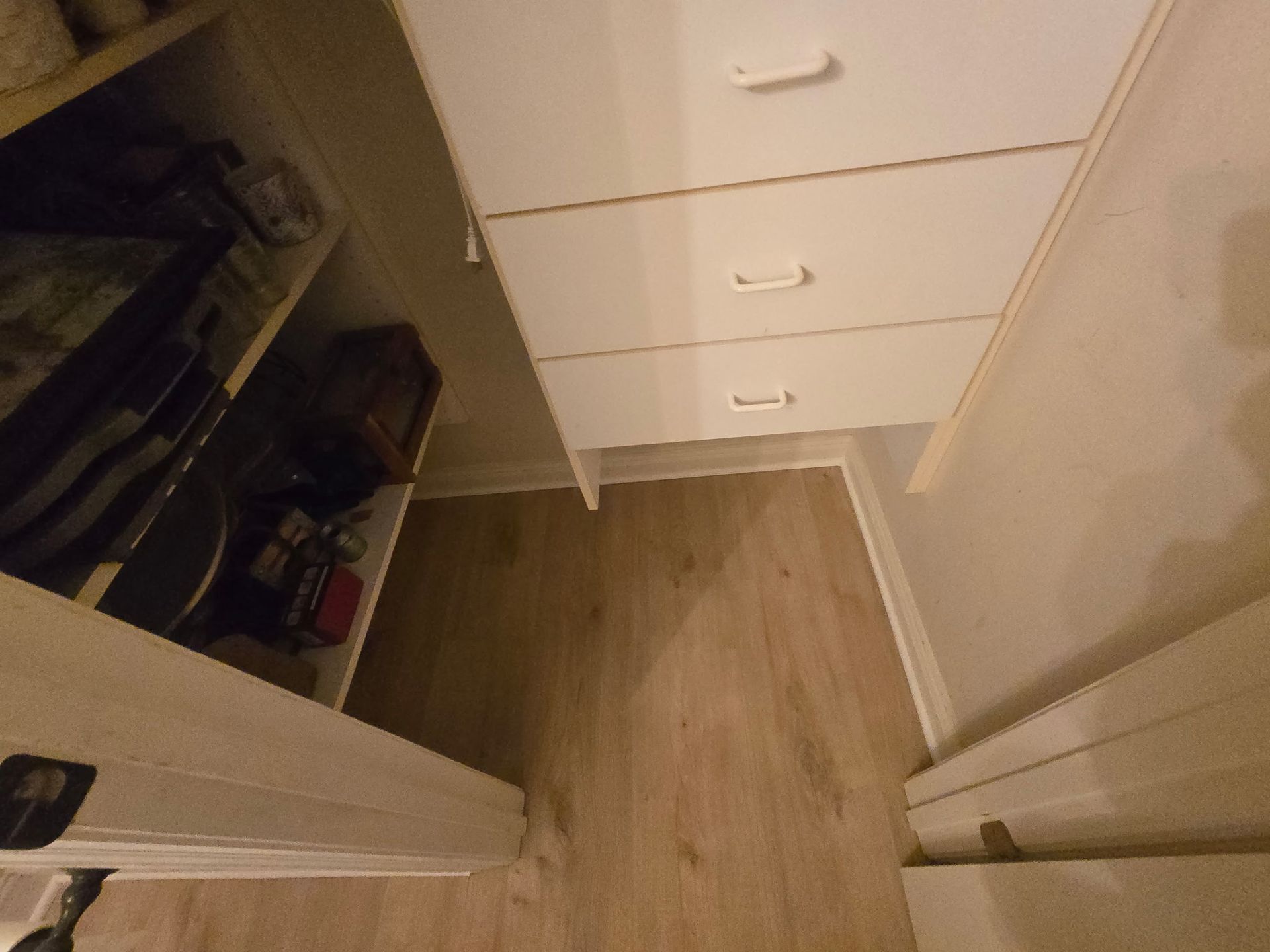 Closet interior with white drawers, shelving, and wooden floors.