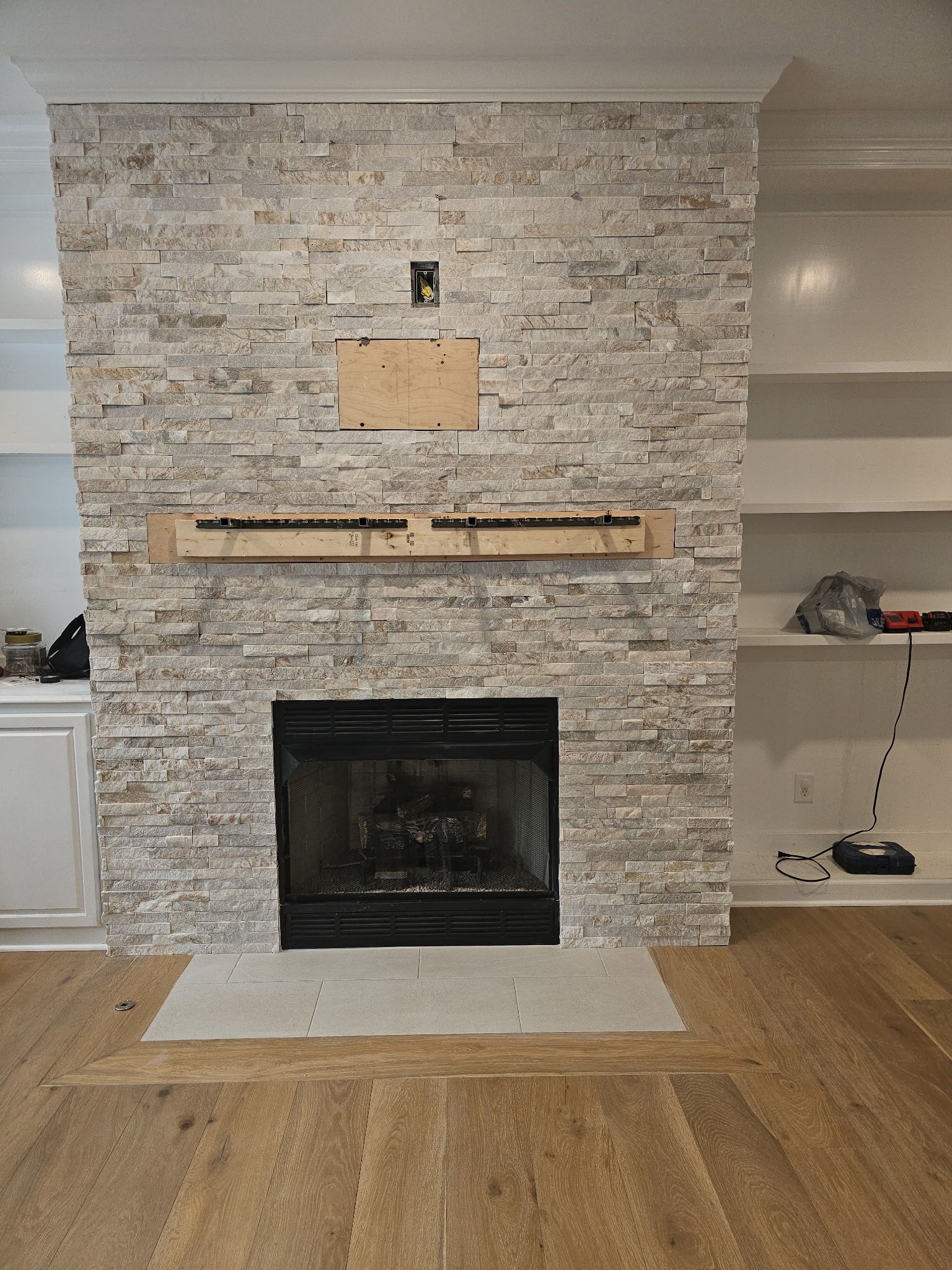 Fireplace with gray stone wall, wood mantel, and hardwood flooring.  Shelves to the right.