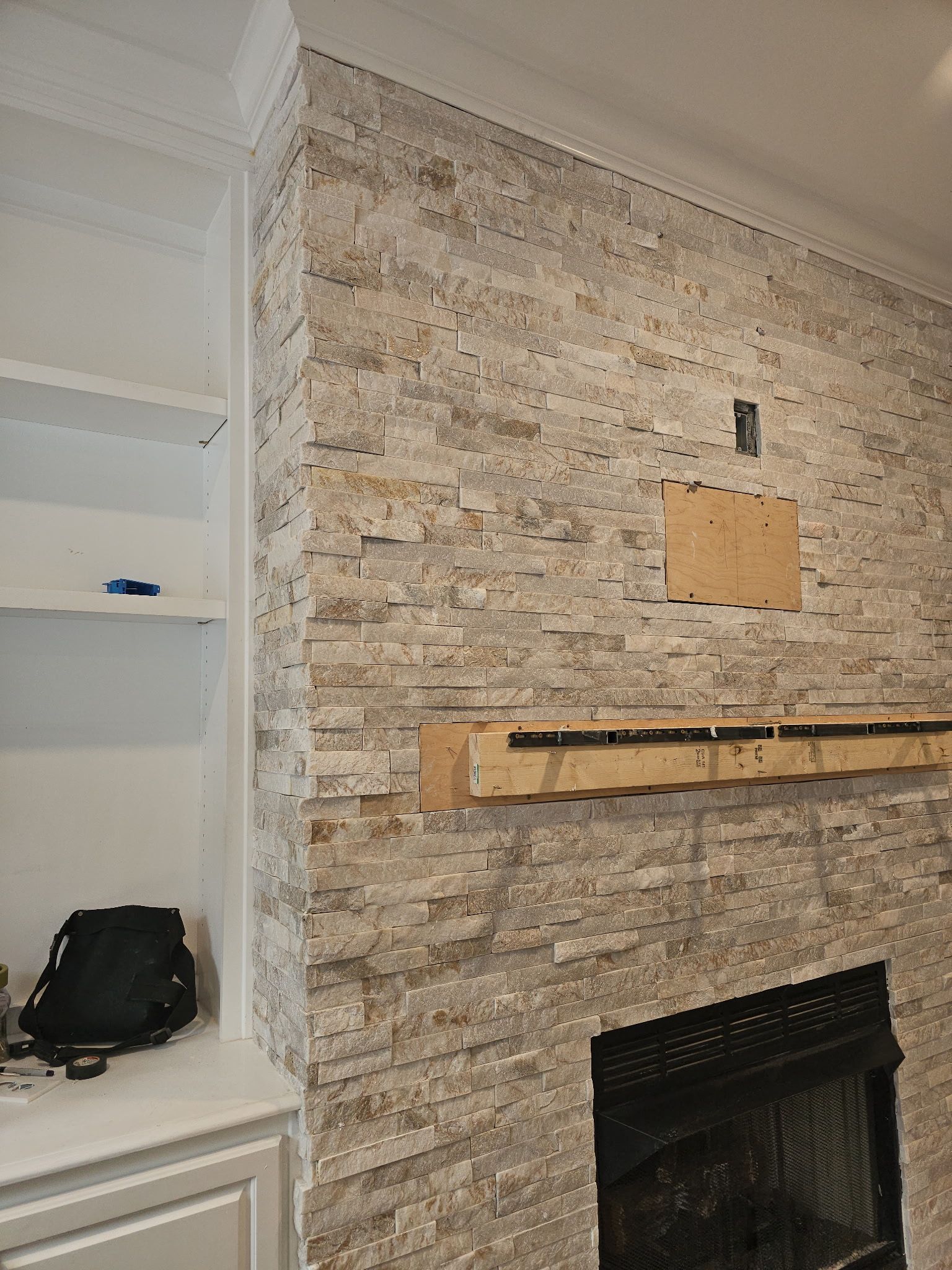 Fireplace with stone veneer, built-in bookshelf, and wooden mantle support.