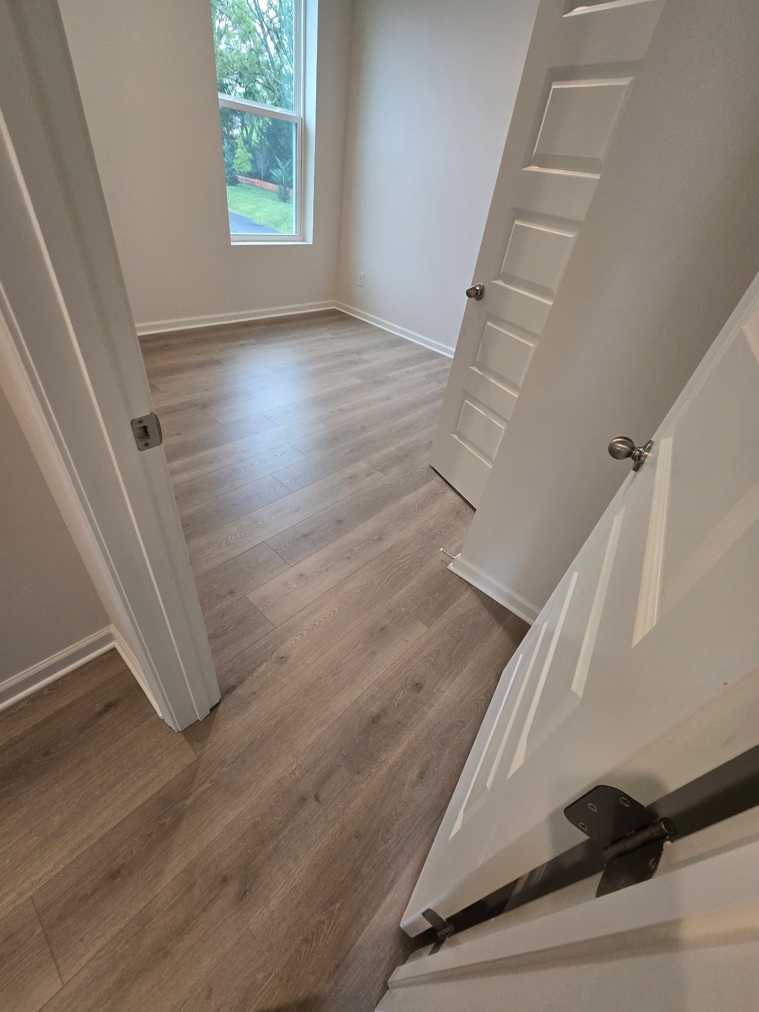A bedroom with hardwood floors, a window, and two white doors slightly ajar.