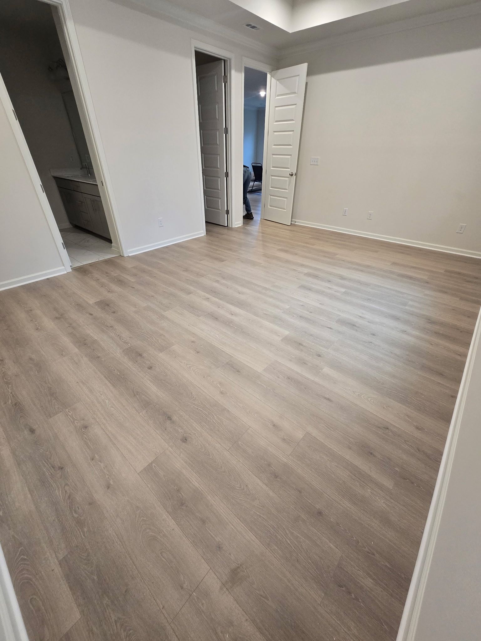 Empty room with light wood-look flooring and white walls. Two doorways lead to other rooms.