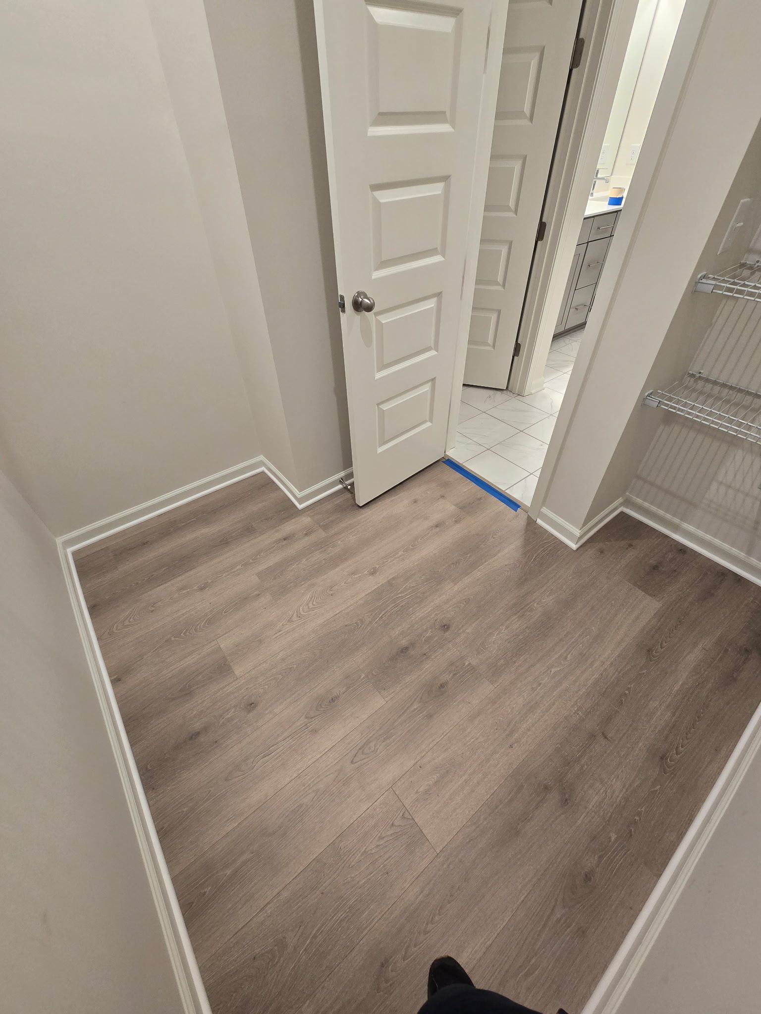 A closet with wood-look flooring, white trim and door, and wire shelving.