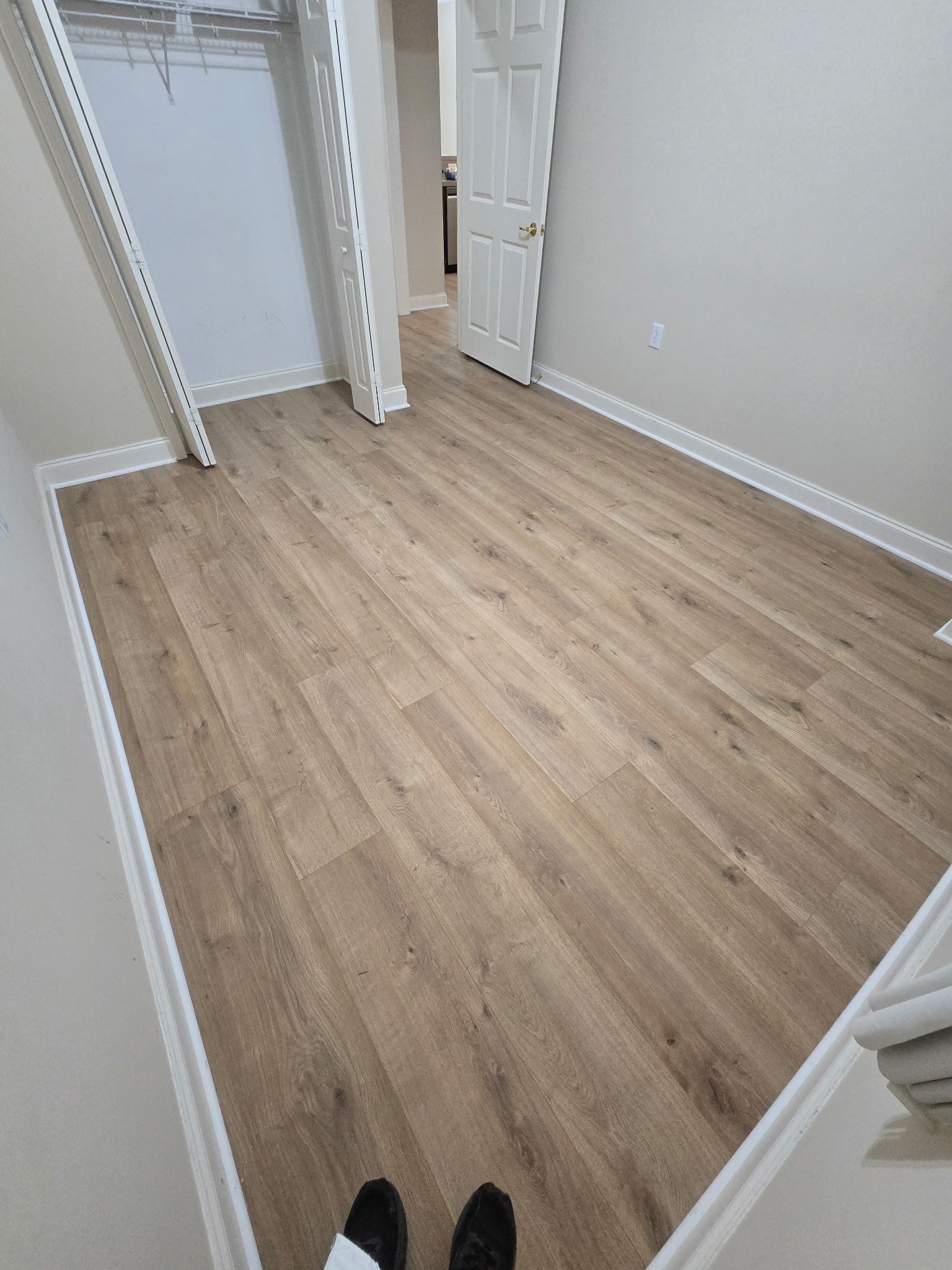 Room with light brown wood-look flooring, white trim, and a closet with a metal shelving system.