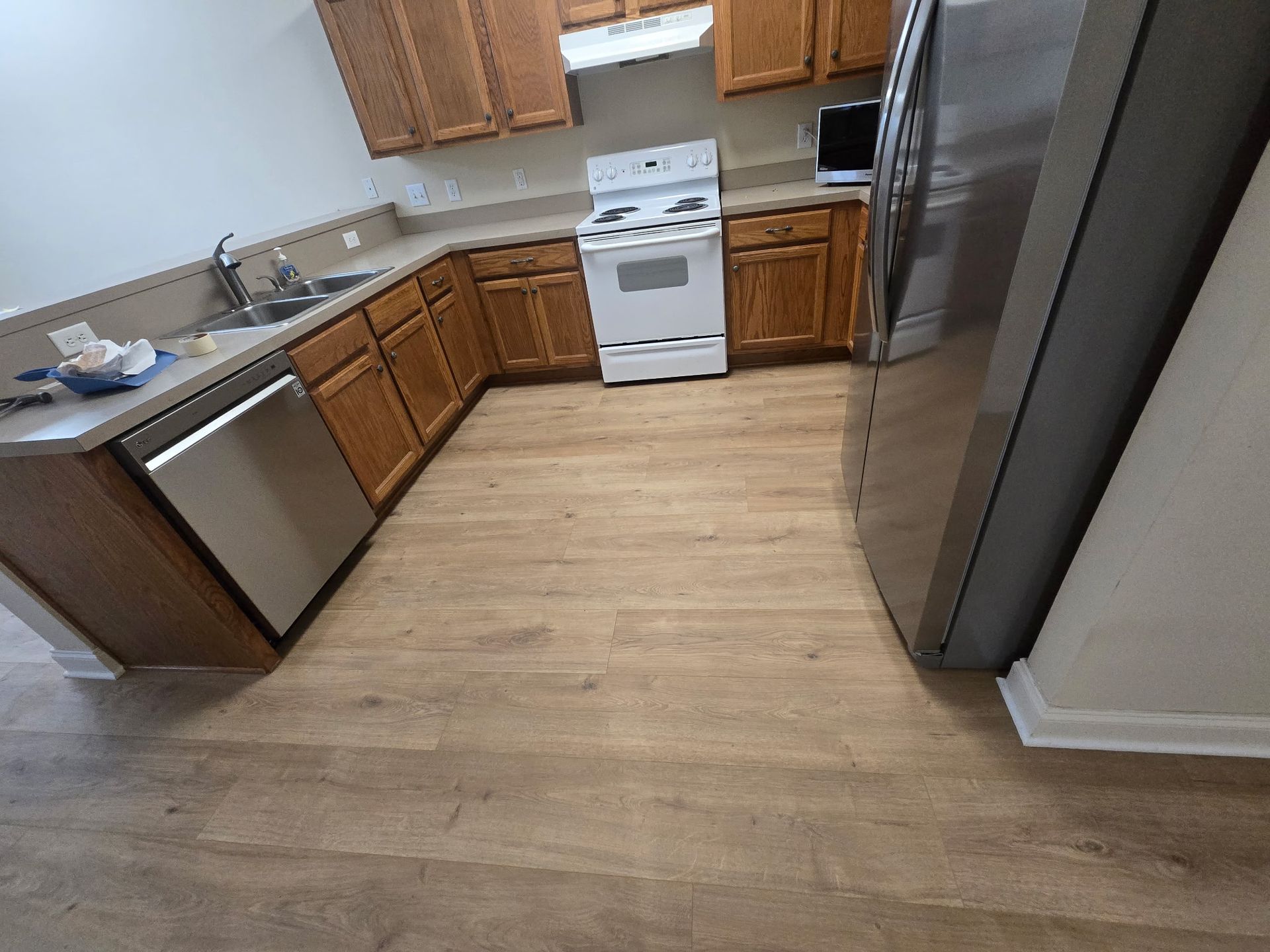 Kitchen with wooden cabinets, white stove, stainless steel appliances, and wood-look flooring.