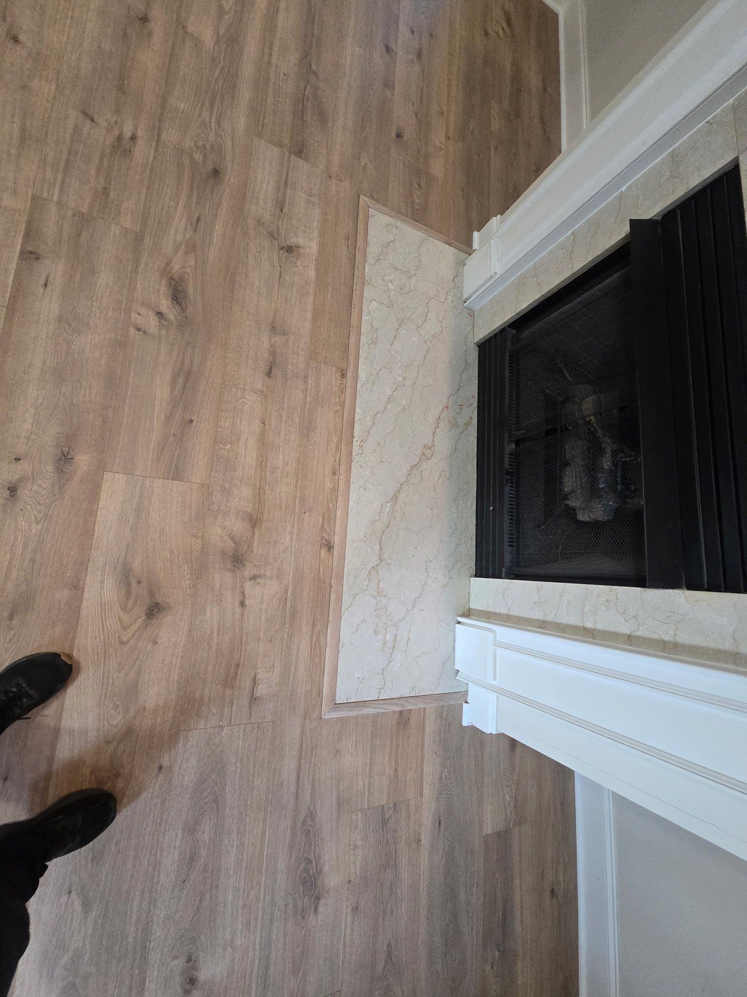 Light wood-look flooring meets a stone hearth and a fireplace with a white mantel.